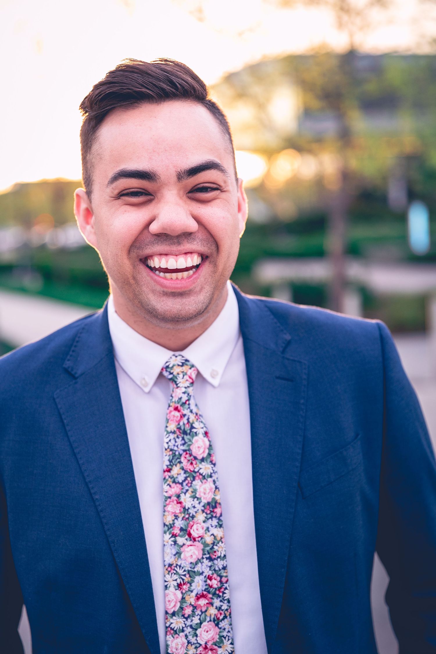 A smiling person in a suit with a floral tie outdoors at dusk, captured by Dillon Workman Photography LLC