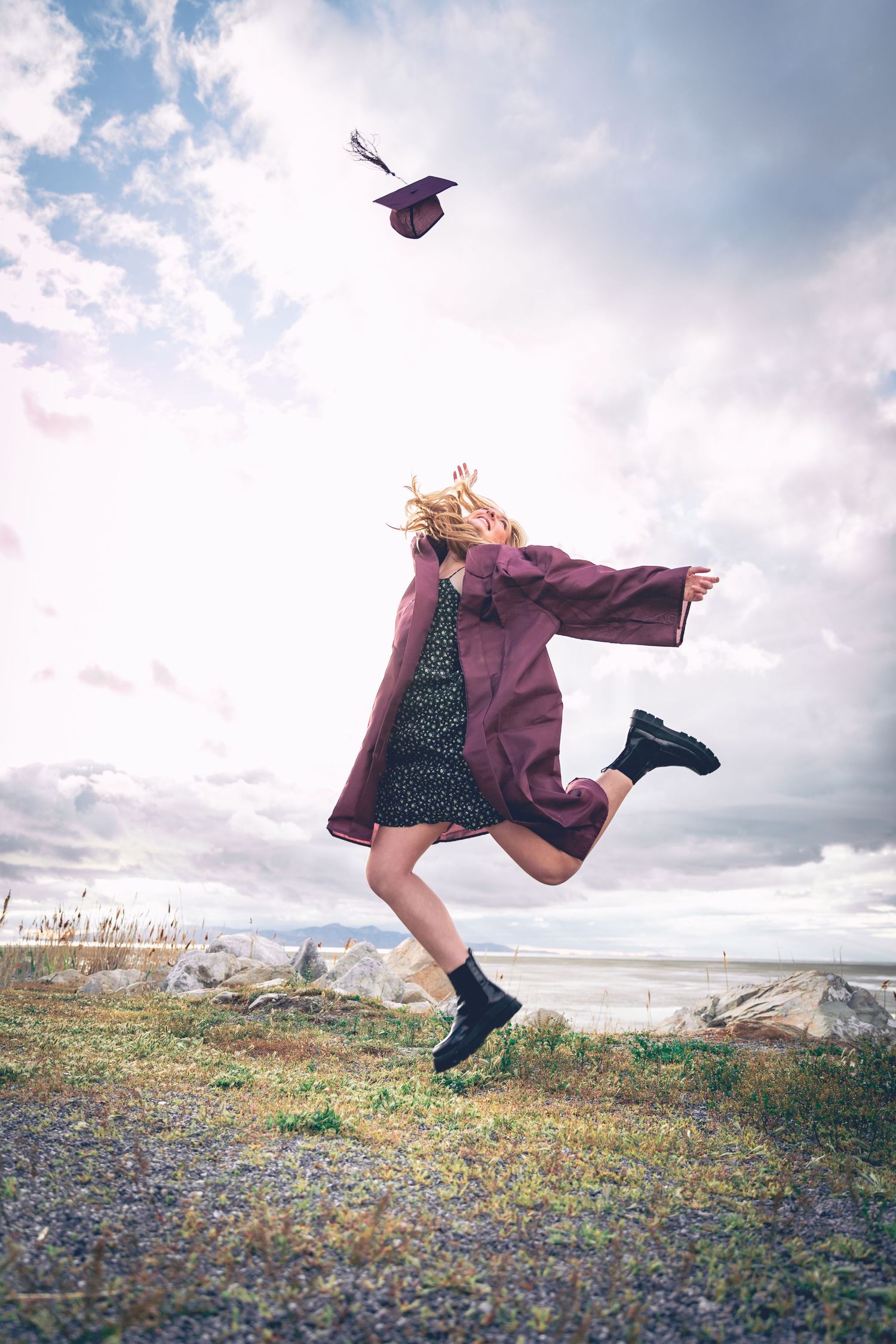 Graduate joyfully tossing cap in the air outdoors during their personalized graduation portraits session.
