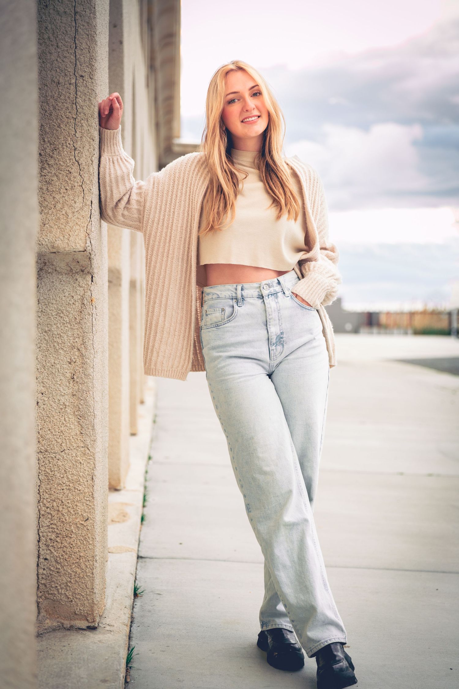 A woman in a cropped sweater and jeans leaning against a wall for her Dillon Workman Photography LLC graduation portraits