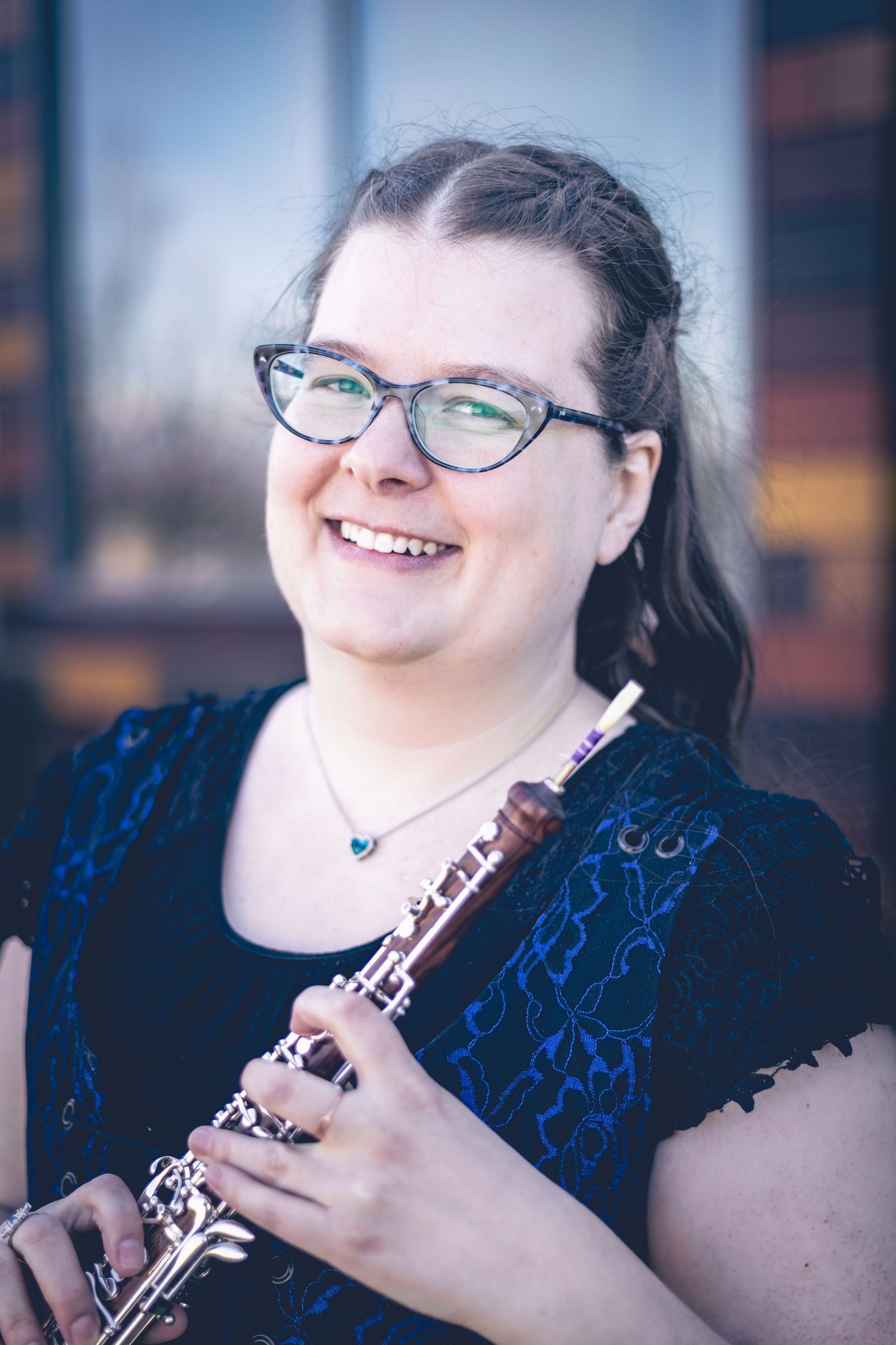 A person with glasses and a dark blue top smiles while holding a woodwind instrument, embodying the charm of musician headshots.