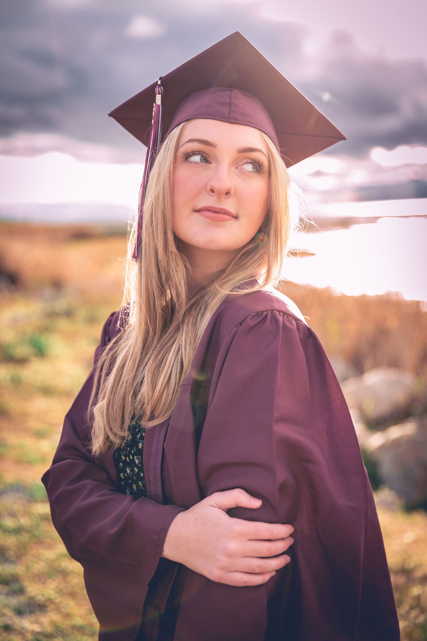A graduate in cap and gown, captured in a personalized photography session, looking contemplatively into the distance.