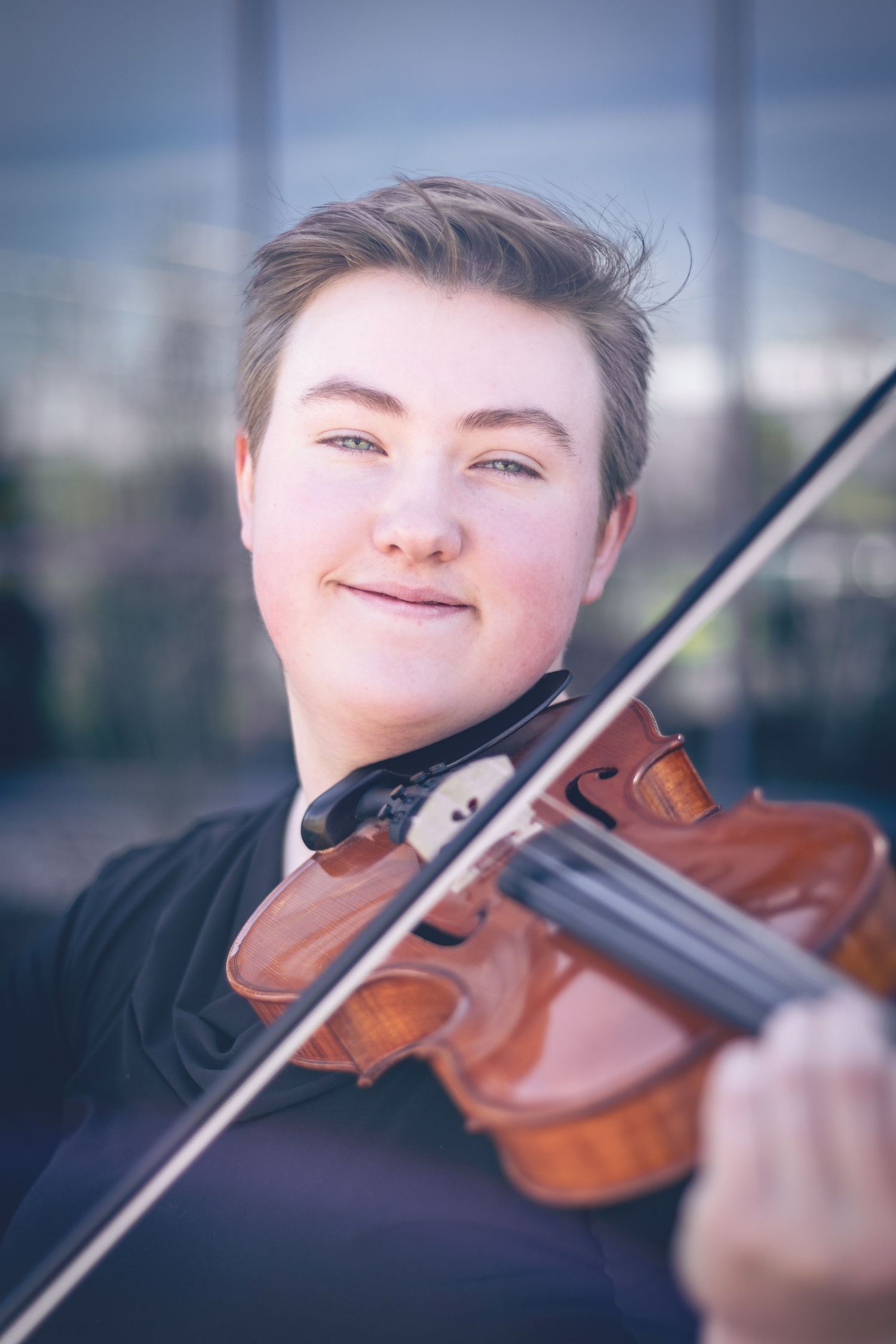 A person with short hair smiles while playing a violin, showcasing a dynamic portrait that captures the essence of musician headshots.