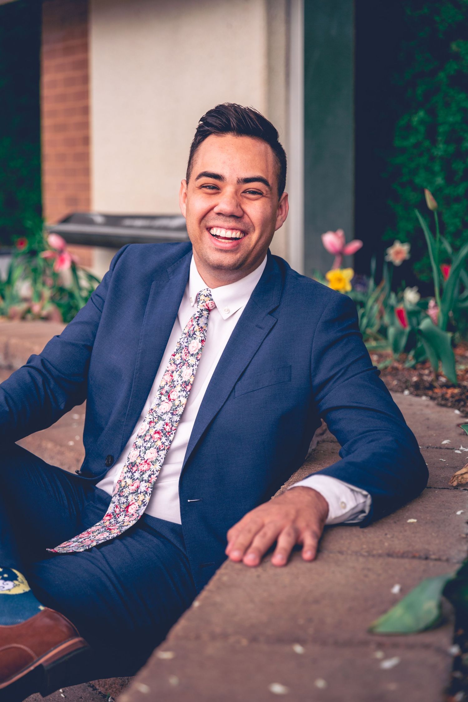 A smiling man in a suit sitting on outdoor steps with tulips in the background for his personalized graduation portraits.