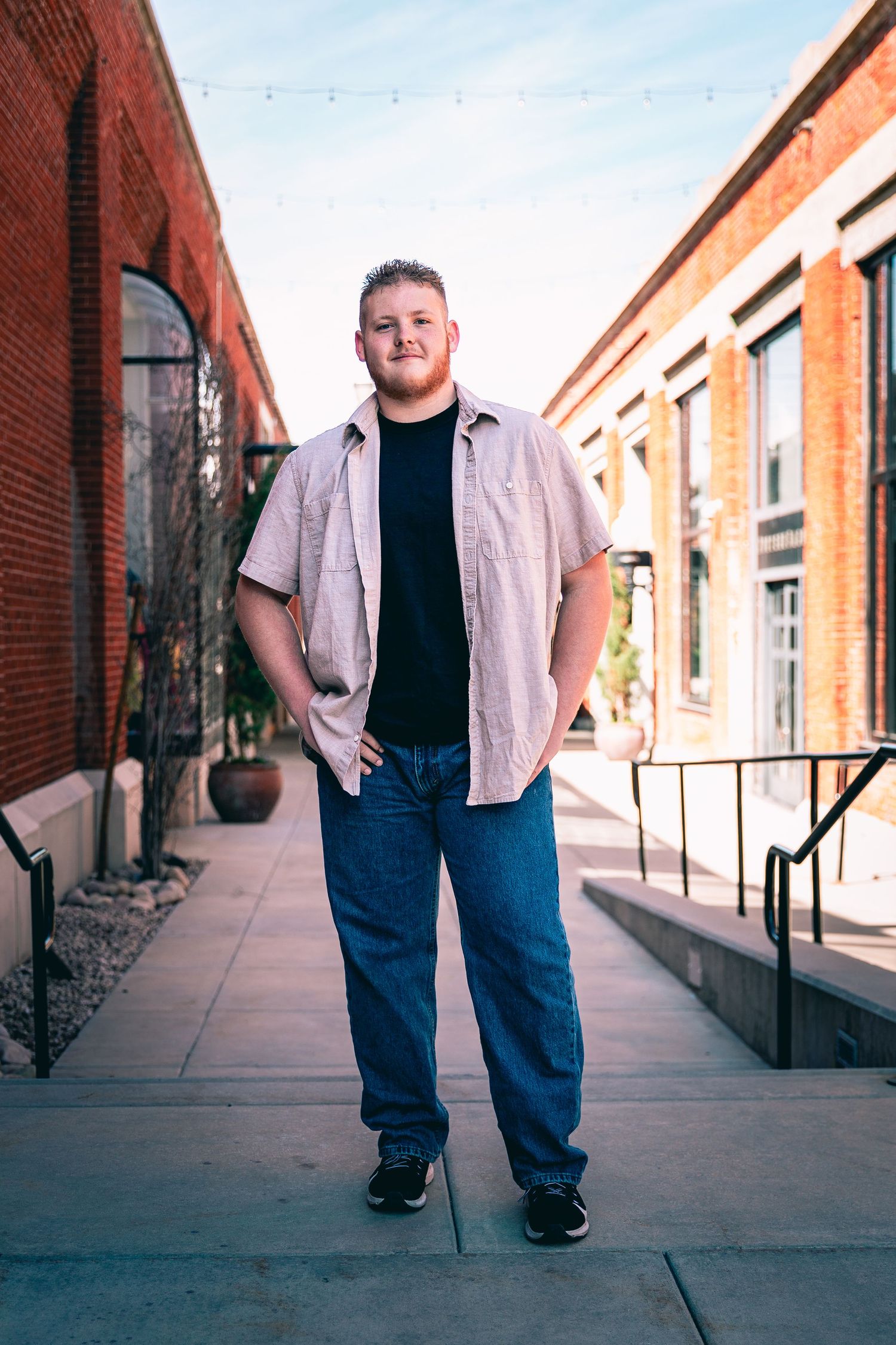 Man standing confidently on a city walkway with hands in pockets for his senior portrait photography session.