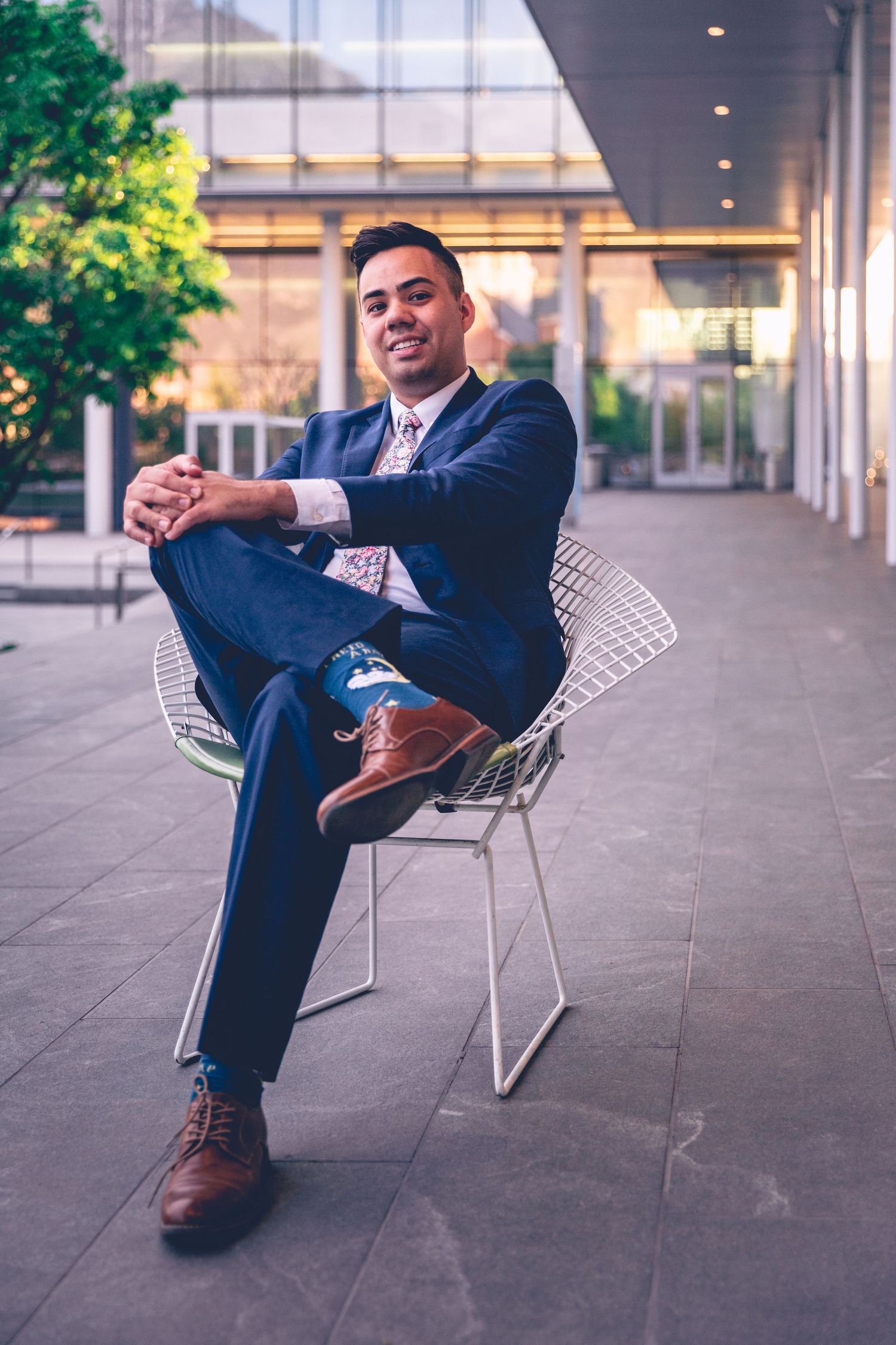 Man in a suit sitting comfortably on a modern wire chair outdoors for his personalized photography college graduation session