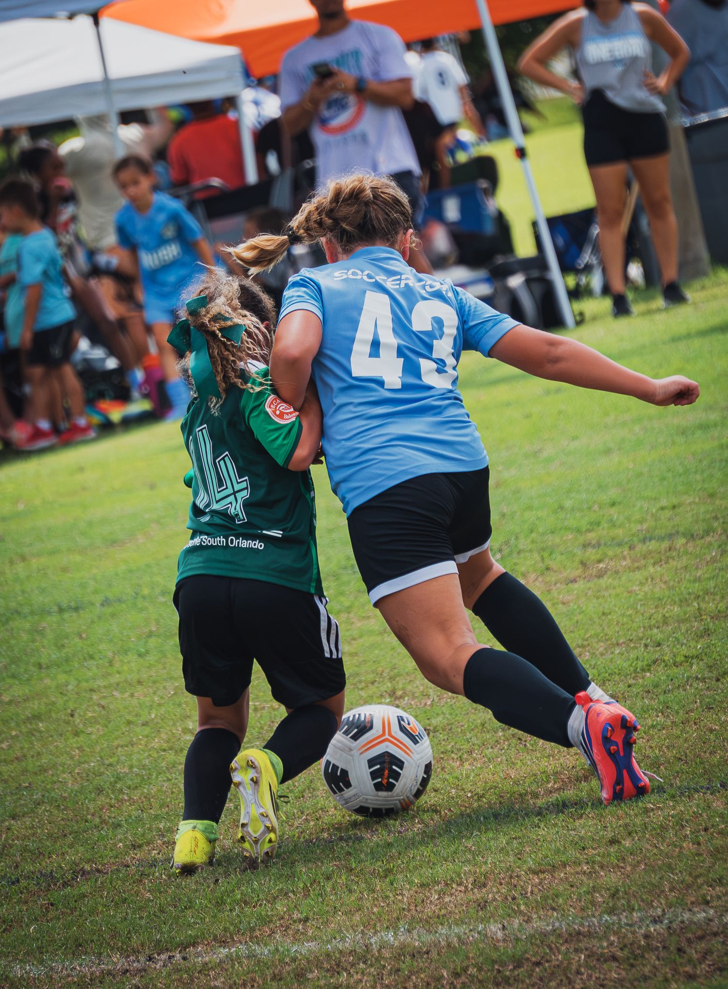 Two female youth soccer players competing for the ball during an outdoor tournament match.