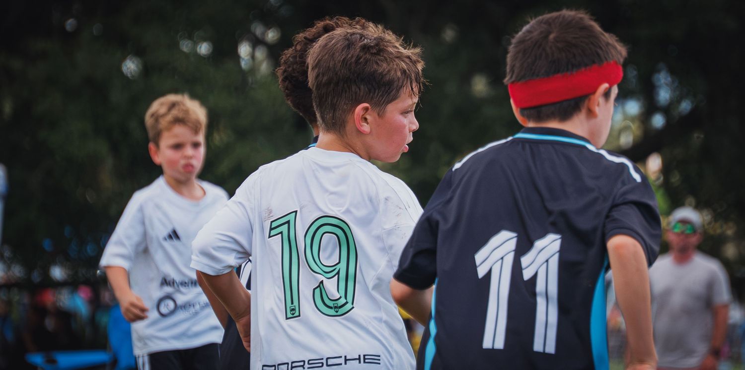 Three youth soccer players in numbered jerseys 19 and 11 standing together at outdoor tournament.