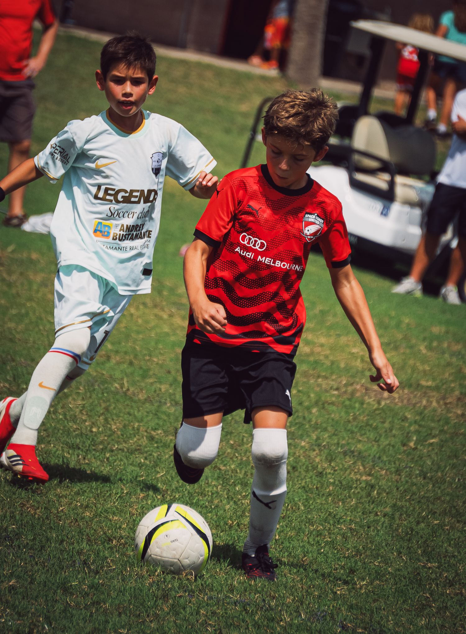 Two youth soccer players compete for the ball during a competitive match on a green grass field.