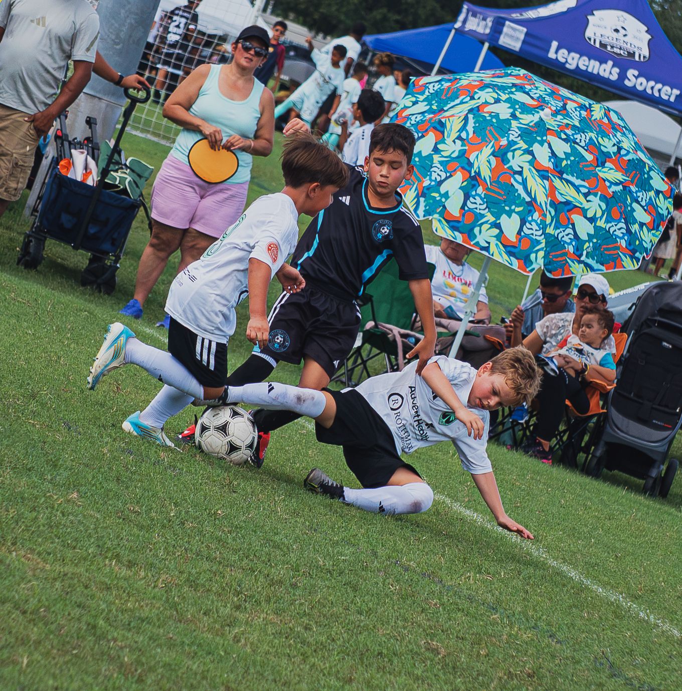 Youth soccer players in intense tackle battle for the ball during competitive outdoor tournament.