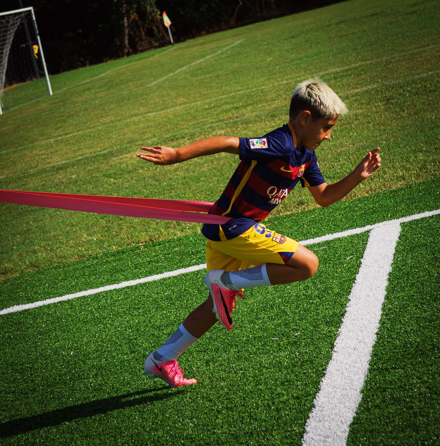 Young blonde soccer player in FC Barcelona kit sprints with resistance band during speed training.