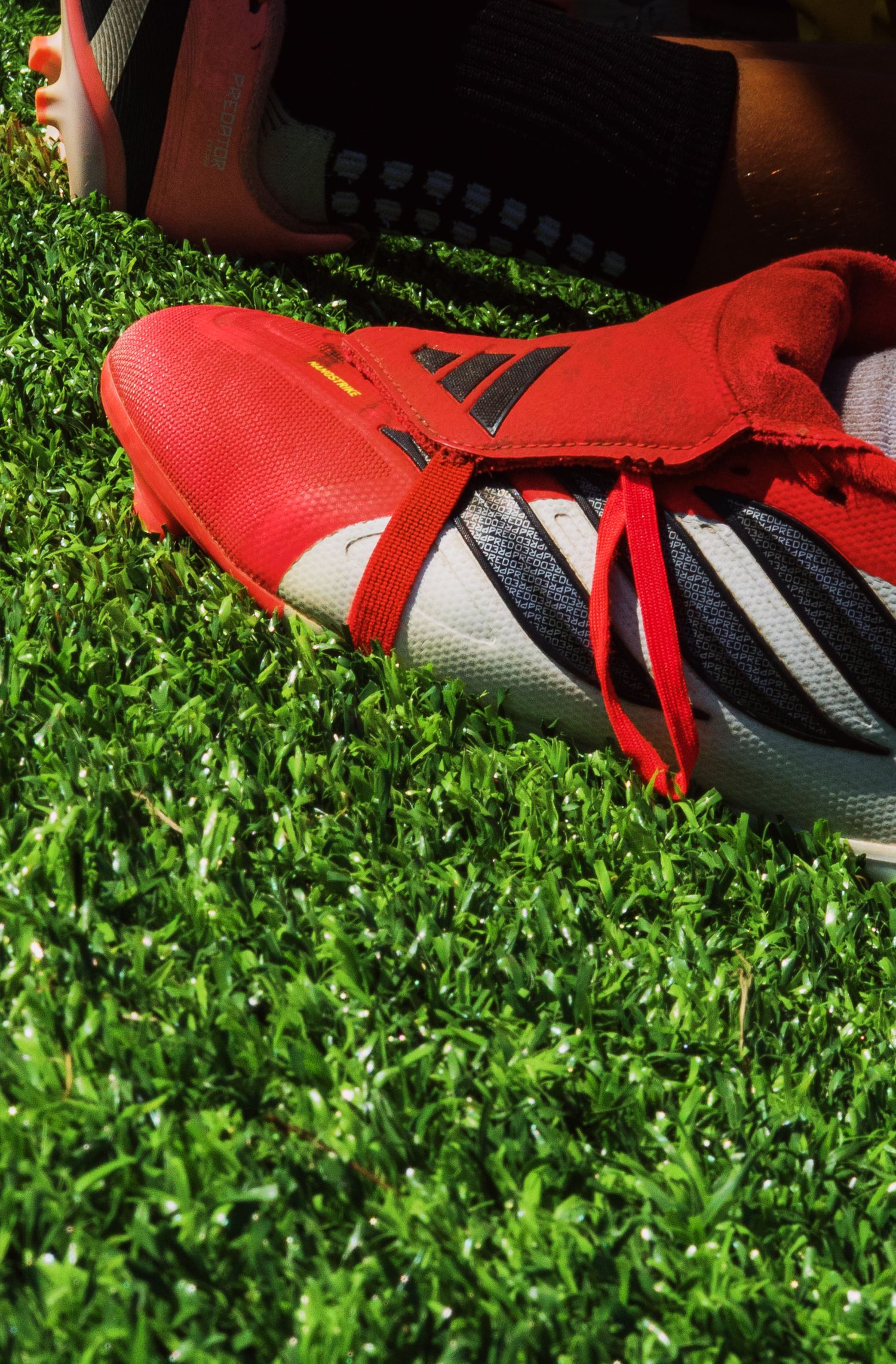 Red and white Adidas soccer cleats with red laces resting on green artificial turf grass.