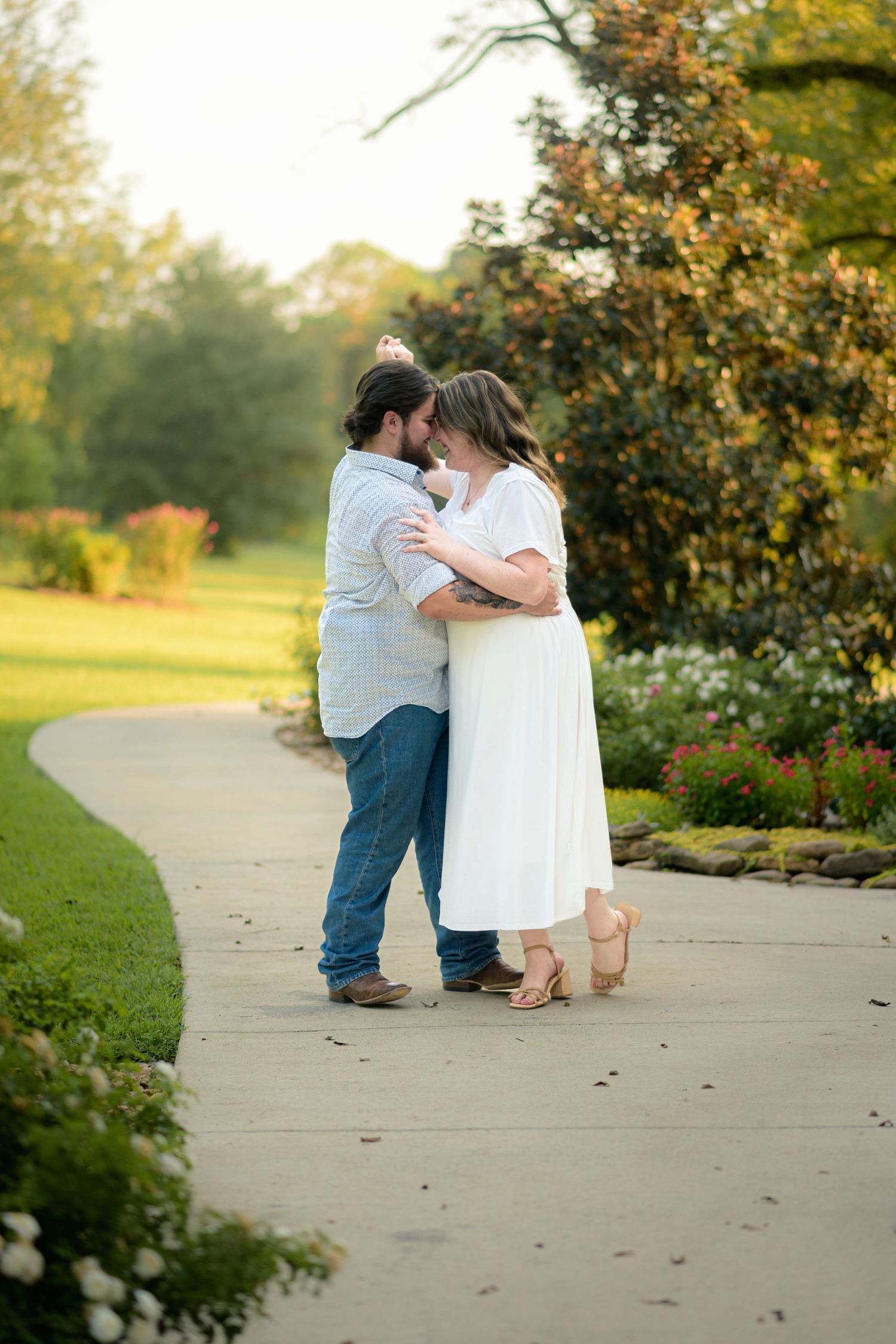 Romantic couple sharing an intimate moment on a garden pathway surrounded by colorful flowers at golden hour.