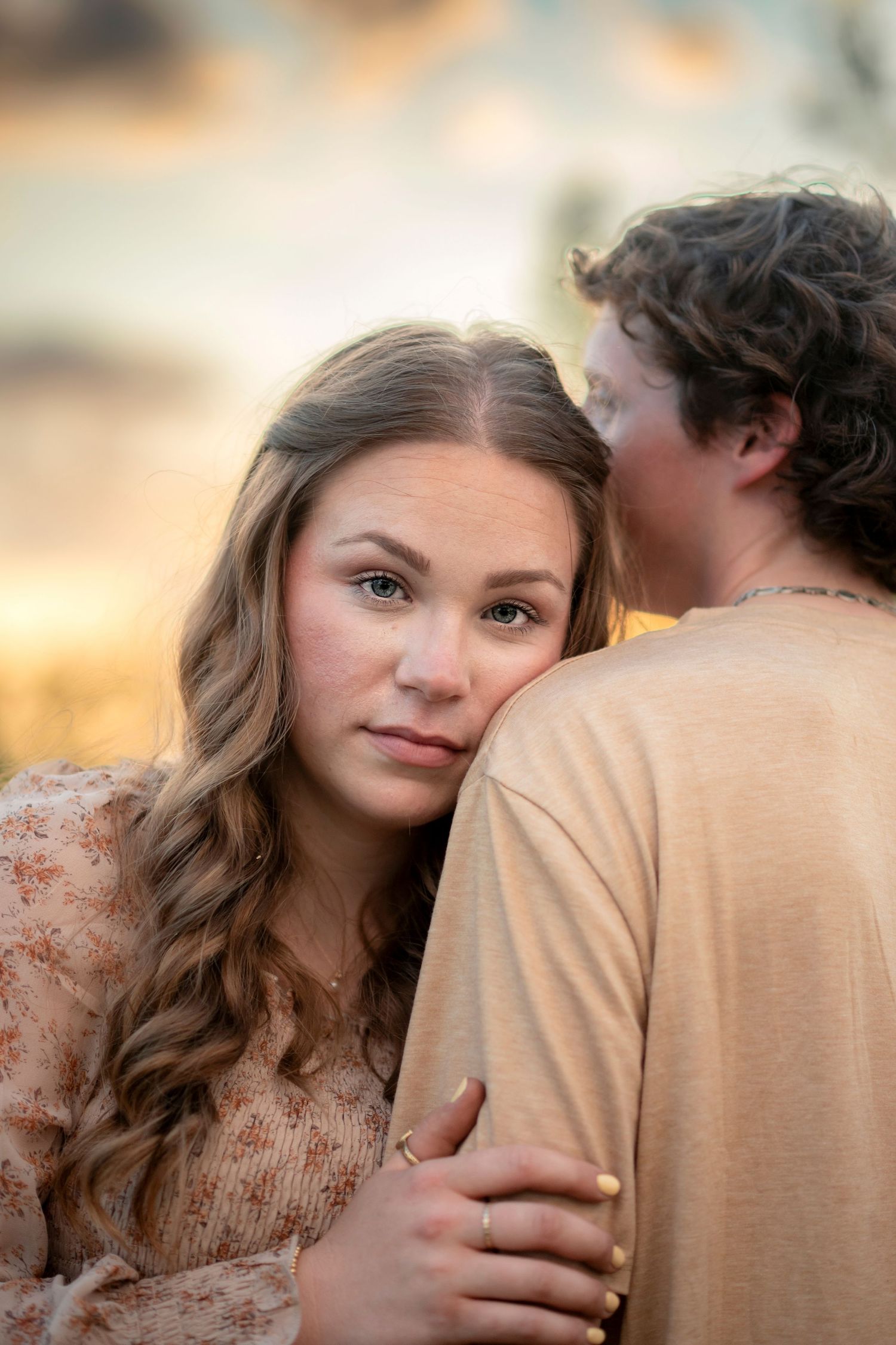 Young woman rests her head on her partner's shoulder during a beautiful golden hour sunset.