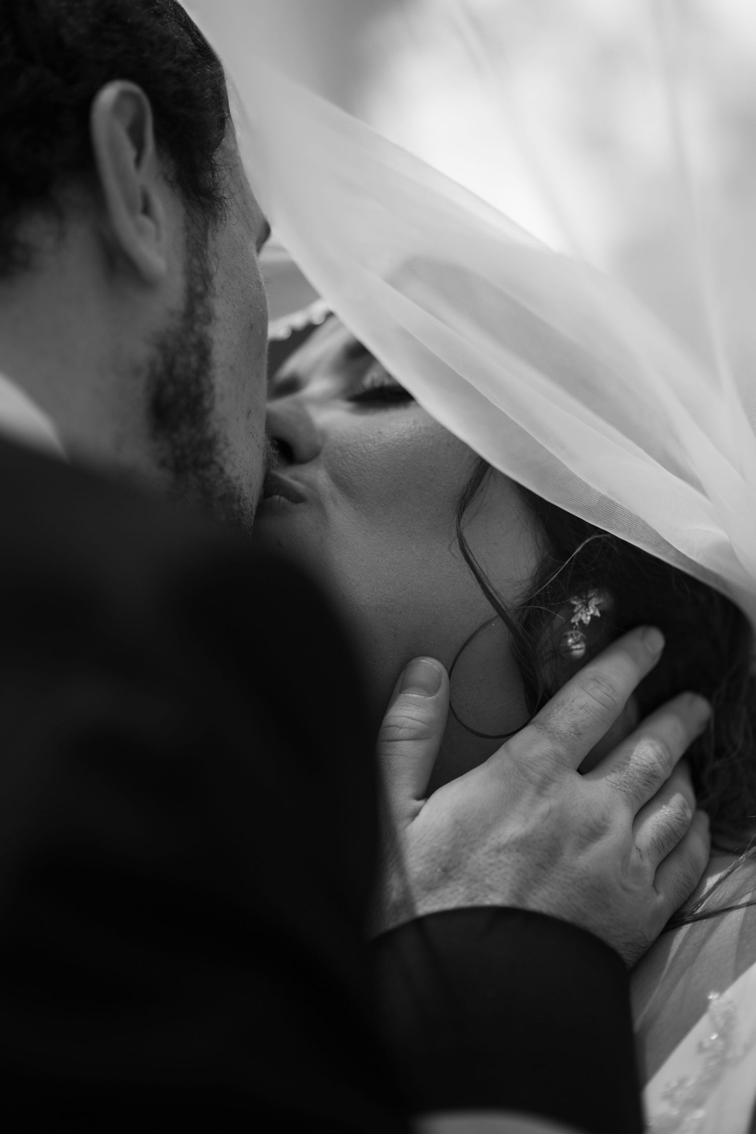 Black and white photo of a groom tenderly kissing his bride under her veil on their wedding day.
