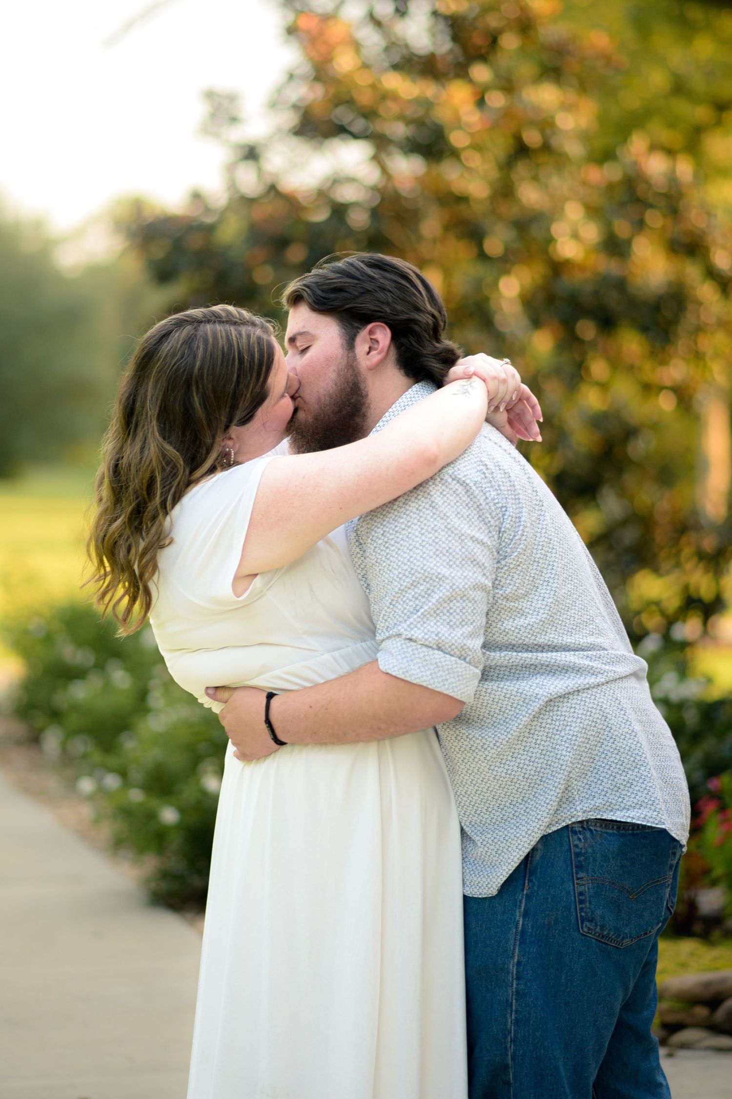 Couple sharing a tender kiss outdoors during a golden hour engagement photo session.