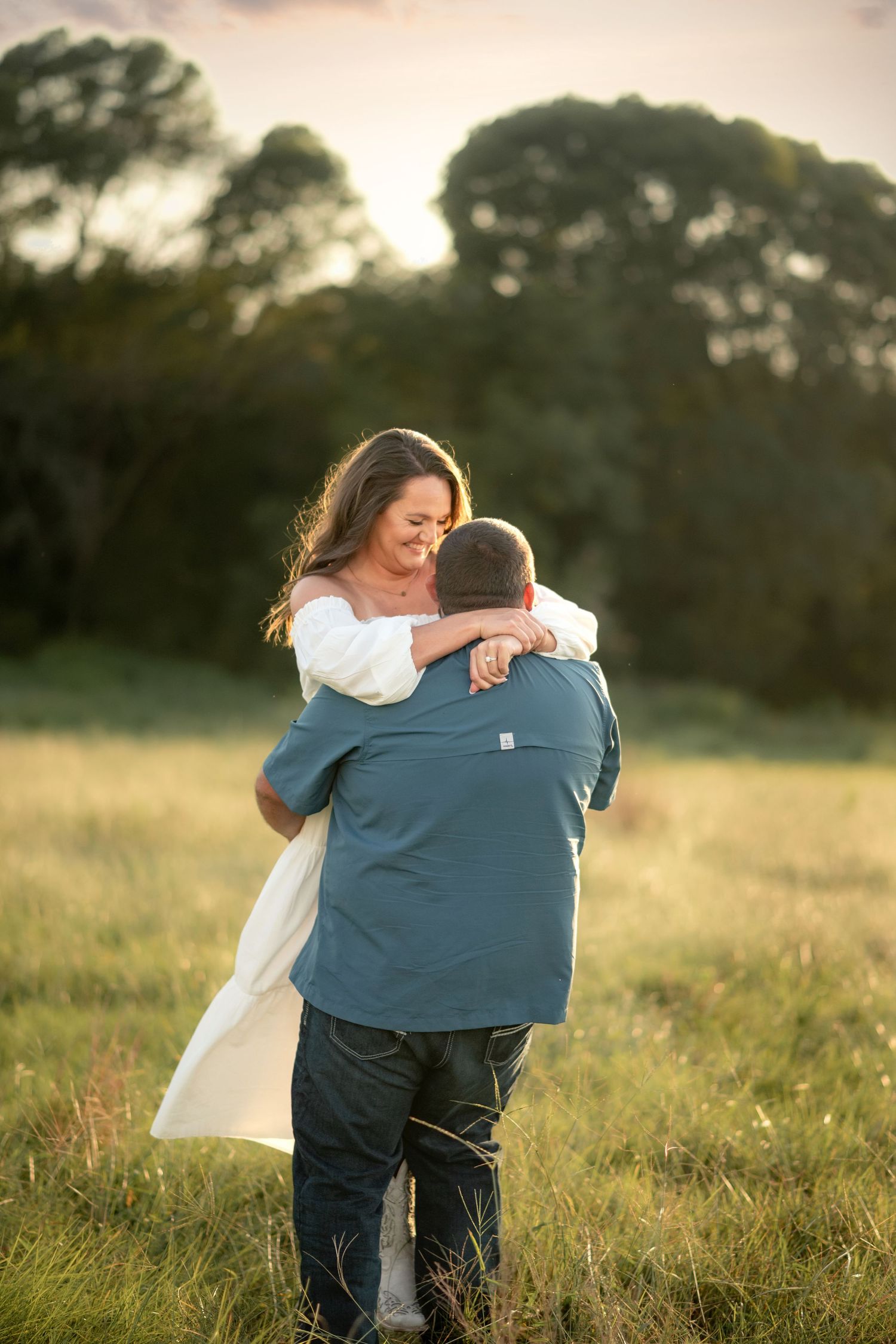 Happy couple sharing a warm embrace in a sunlit grassy field during a beautiful golden hour session.