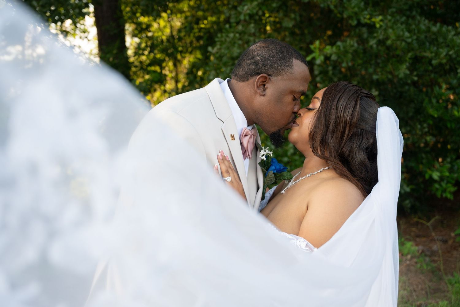 Bride and groom sharing a romantic kiss wrapped in a flowing white veil outdoors.