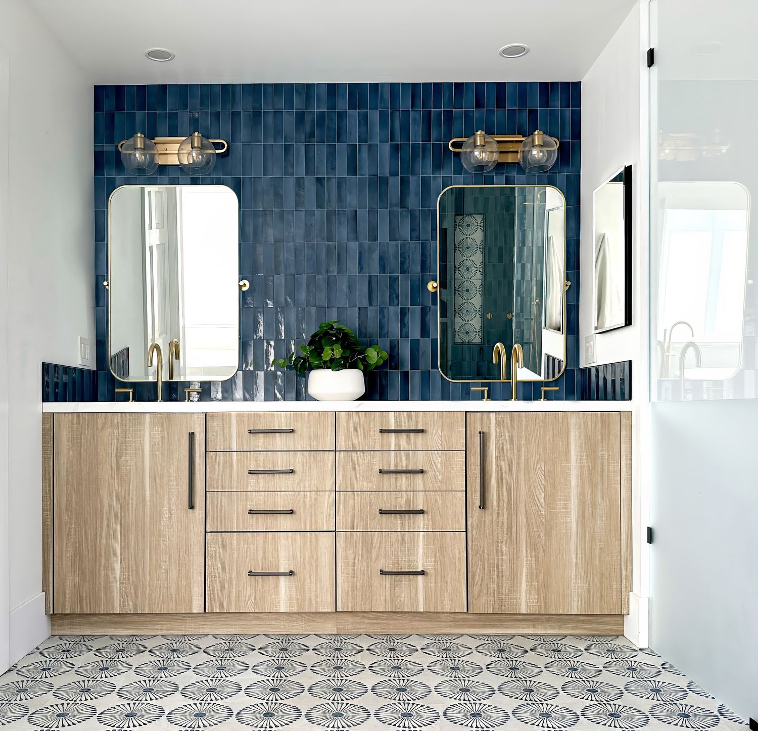 Wide view of modern bathroom with blue tile backsplash and light wood cabinetry.
