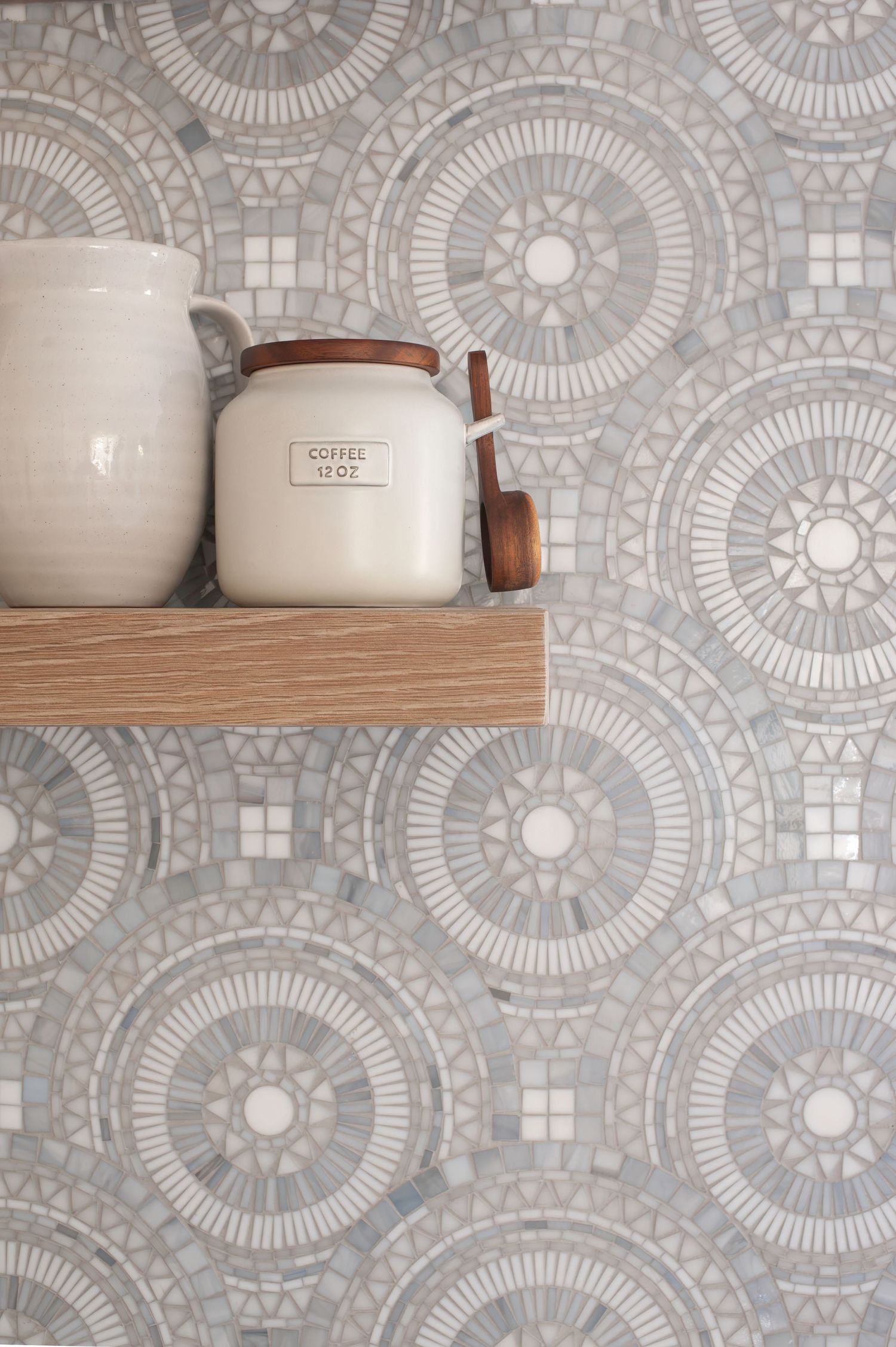 Ceramic storage jars displayed on wooden shelves against a mosaic tile backsplash with circular patterns.