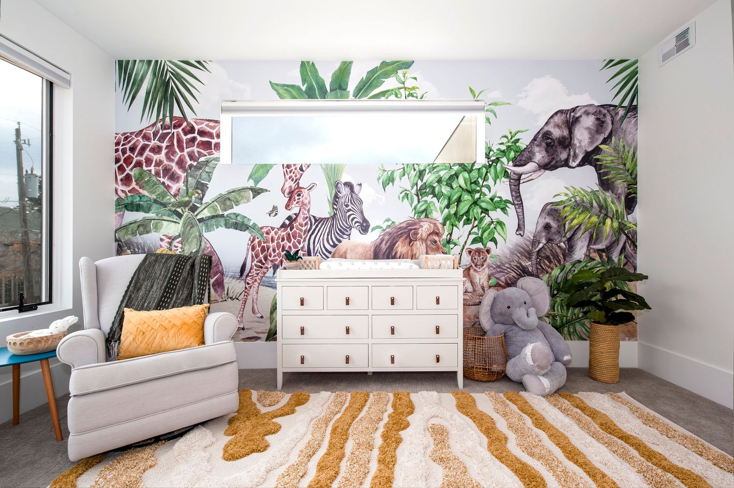 Bright nursery room with white dressers, tropical wallpaper, and natural fiber baskets.