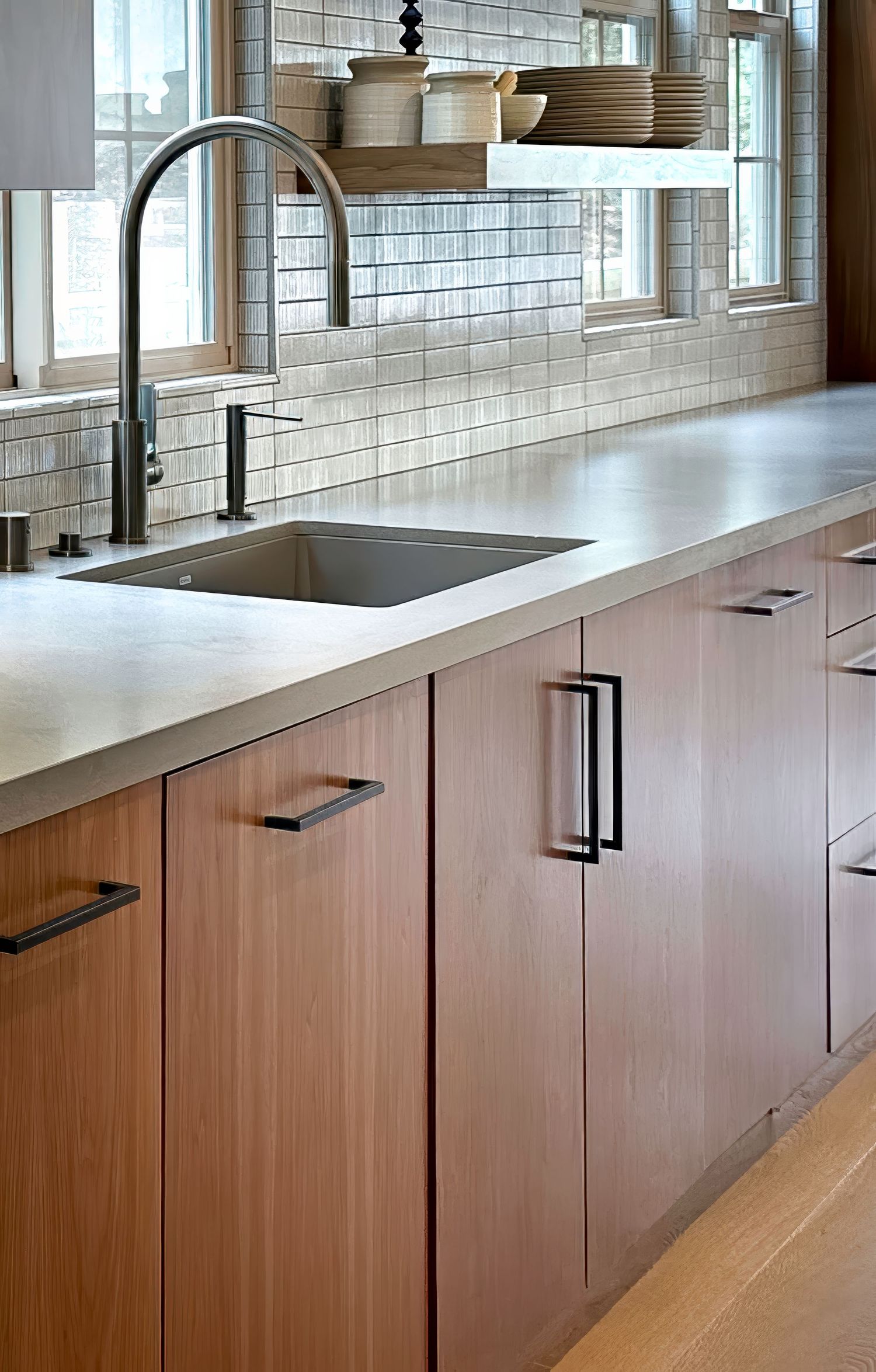Sleek kitchen cabinetry with wooden finish and black hardware against soft blue tile backsplash.