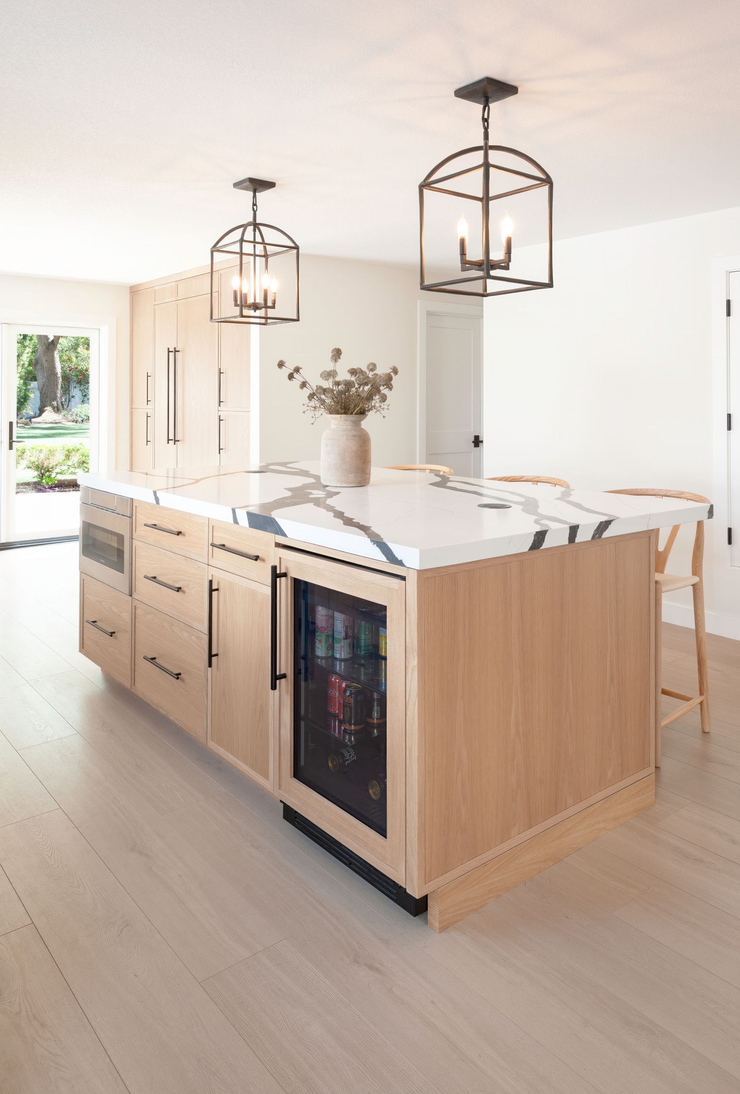 Light-filled kitchen with wood cabinets, island, and modern pendant lighting fixtures.