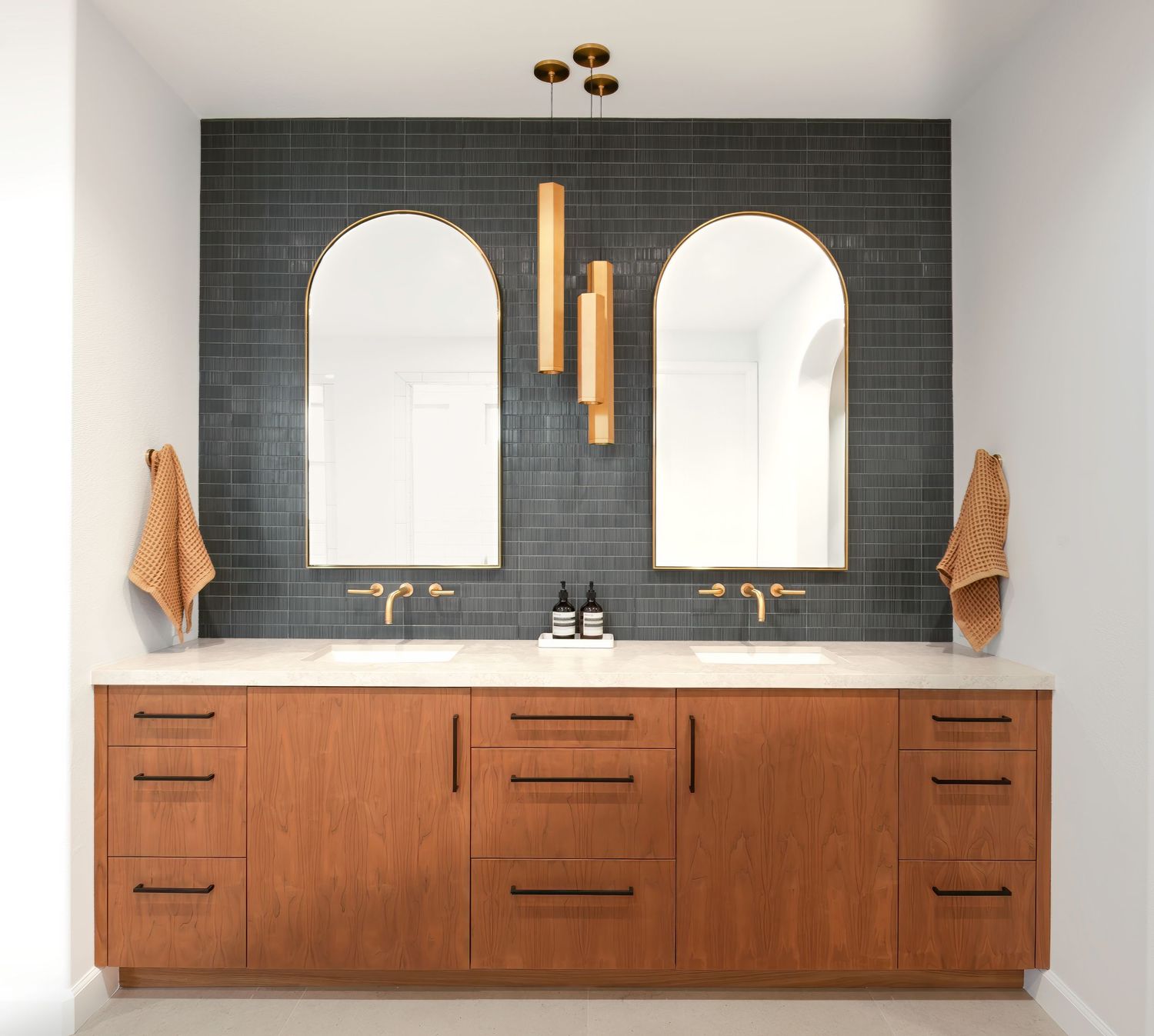 Sleek bathroom vanity with wood cabinets and black tile accent wall featuring arched mirrors.