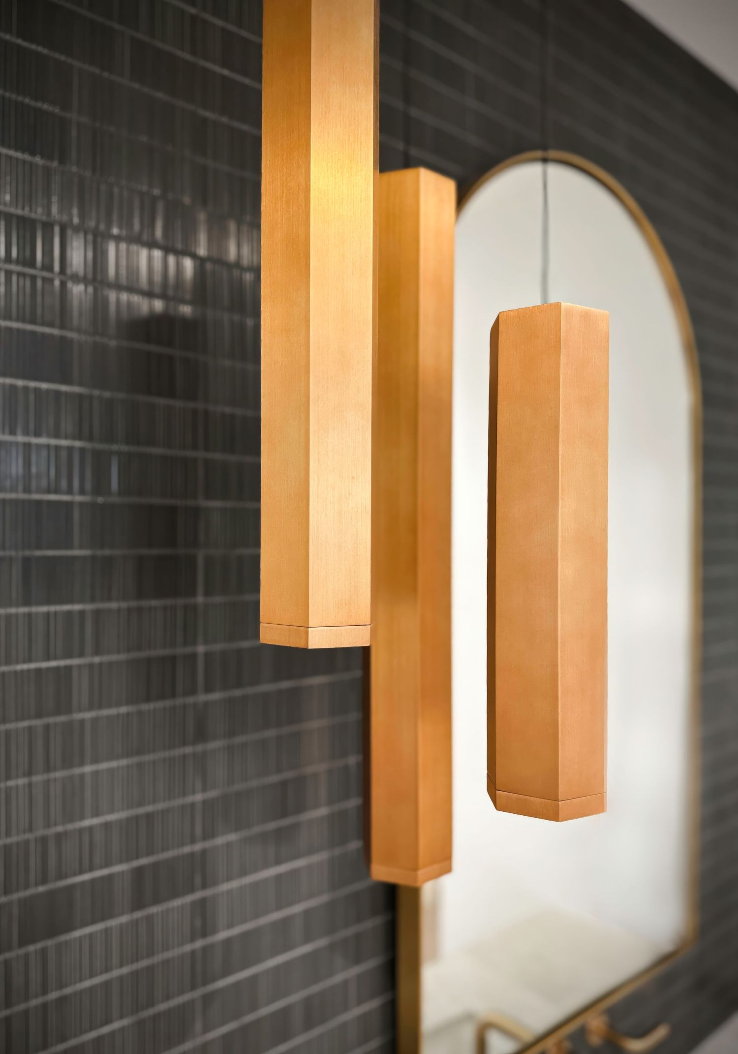 Architectural photo of a vignette of modern bathroom pendants asymmetrically set against dark tile wall with arched mirrors. Moody bathroom