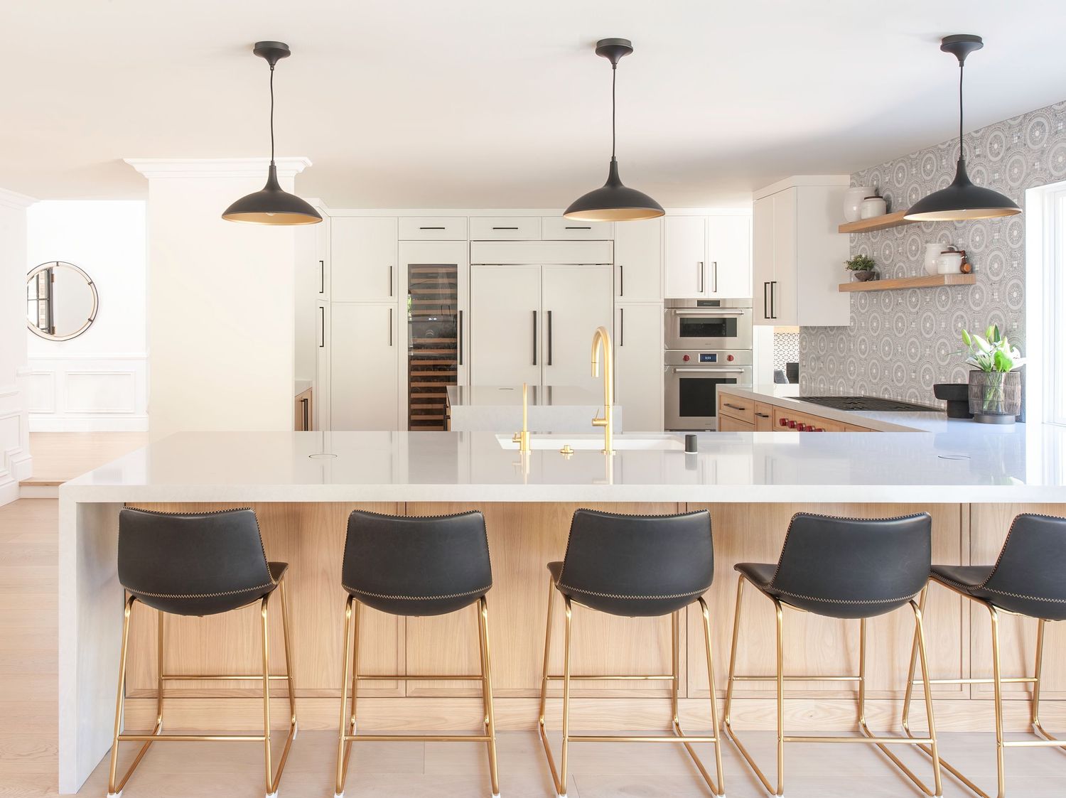 Row of black bar stools along white kitchen counter with pendant lighting.