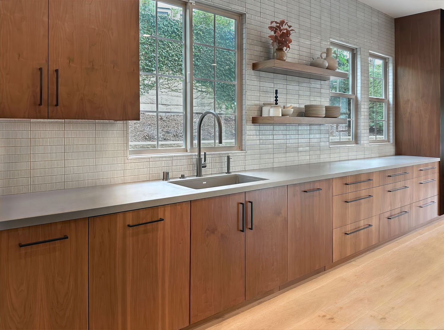 Long view of modern kitchen with wood cabinets, white countertops, and subway tile backsplash.