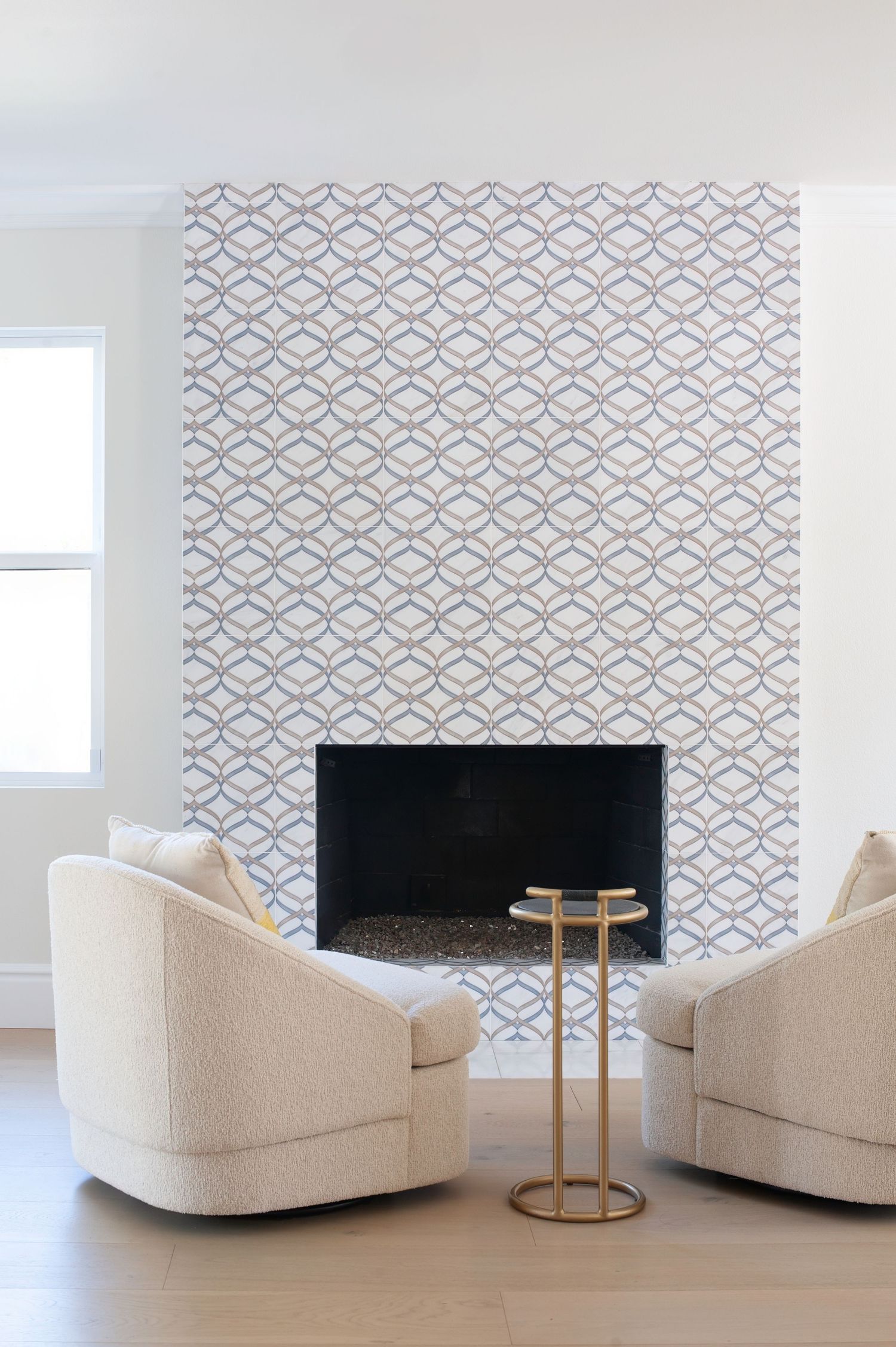 Interior vignette of contemporary living room with cream curved chairs and geometric tile pattern surrounding a modern fireplace.