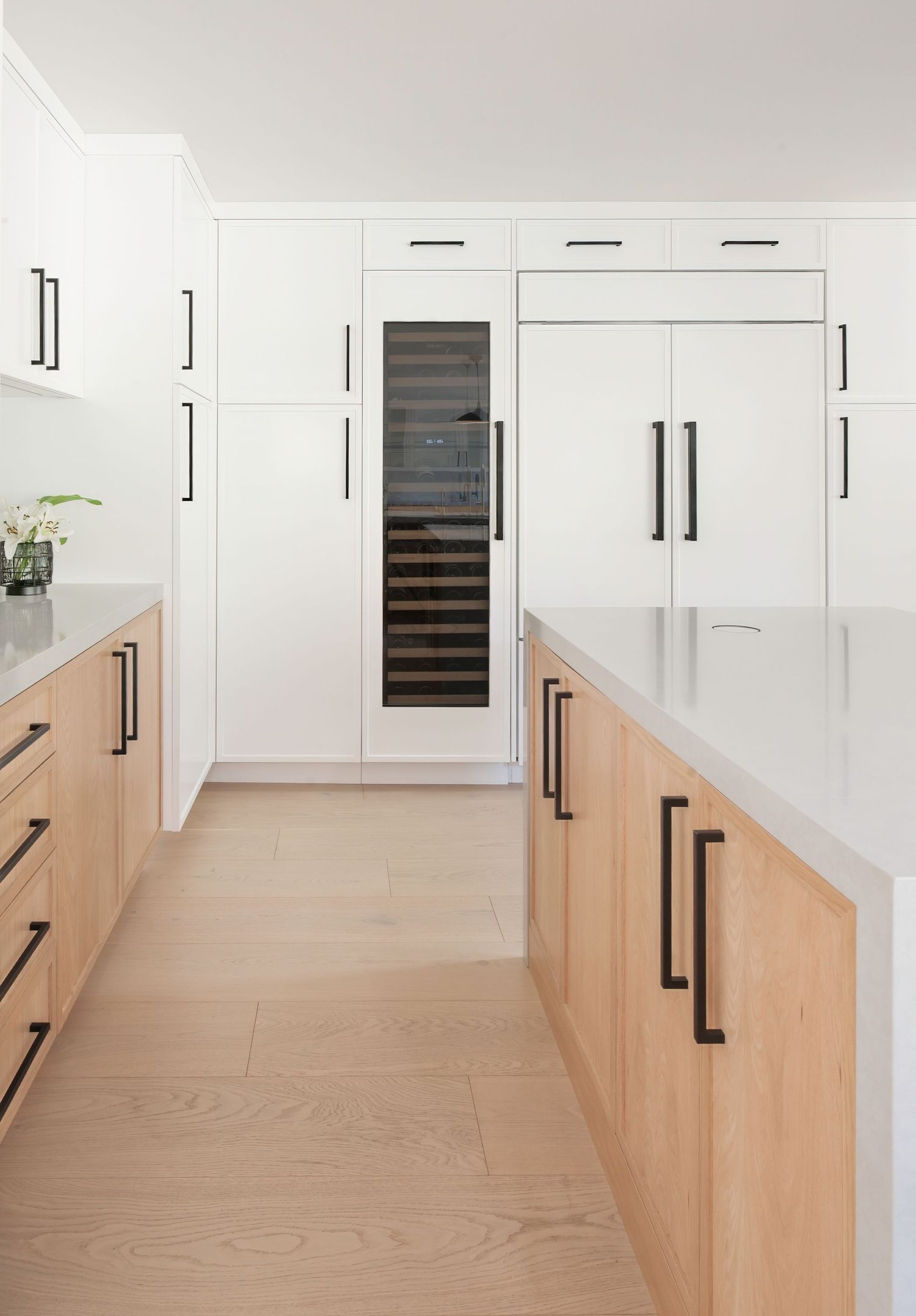 Interior photography of custom kitchen with white upper cabinets and light wood lower cabinets featuring black handles in Southern CA.