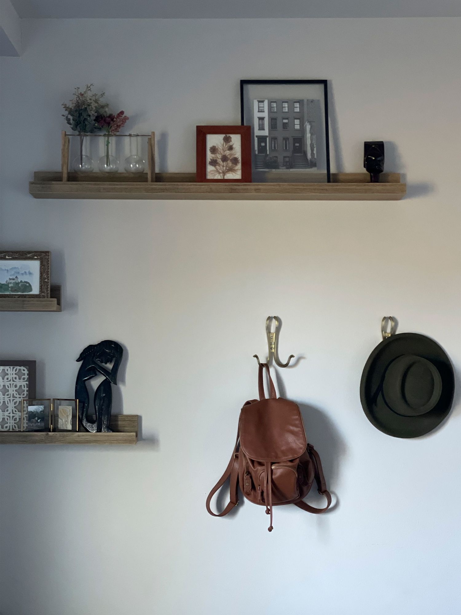 Rustic floating shelves decorated with frames, plants, and a brown leather backpack with green hat.