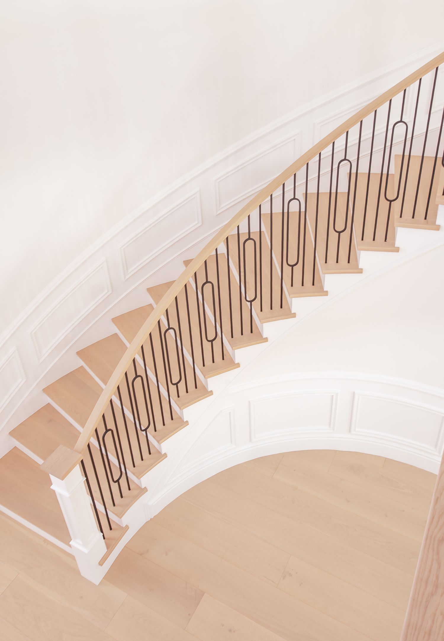 Architectural photo of updated curved white staircase with wooden steps and black metal railings in modern design in Souther California.