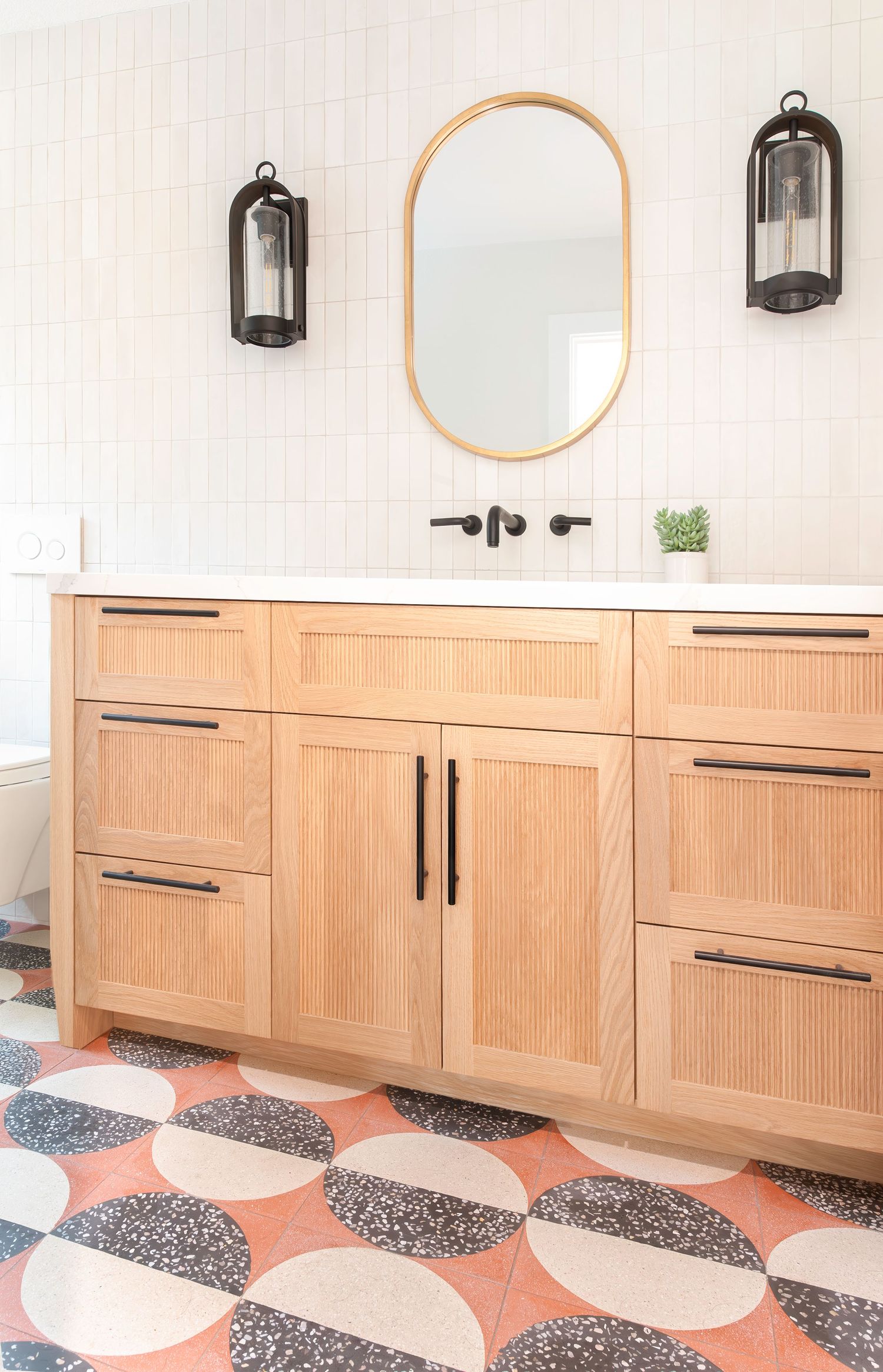 Modern bathroom with reeded cabinetry, patterned terrazzo floor tiles, black fixtures, and brass oval mirror, photographed in SoCal