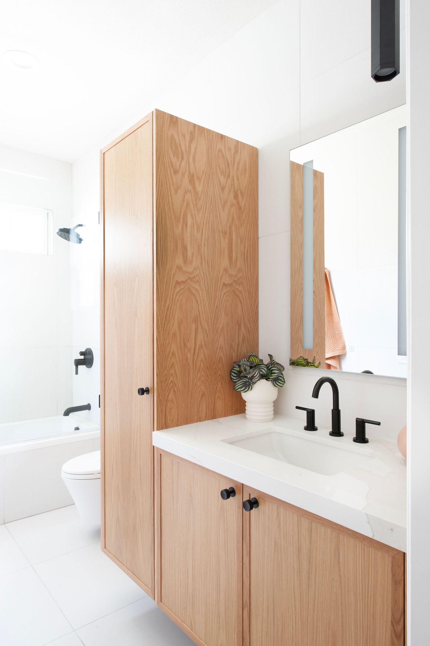Contemporary bathroom featuring wooden cabinetry, black faucets, and a white countertop with minimalist design.