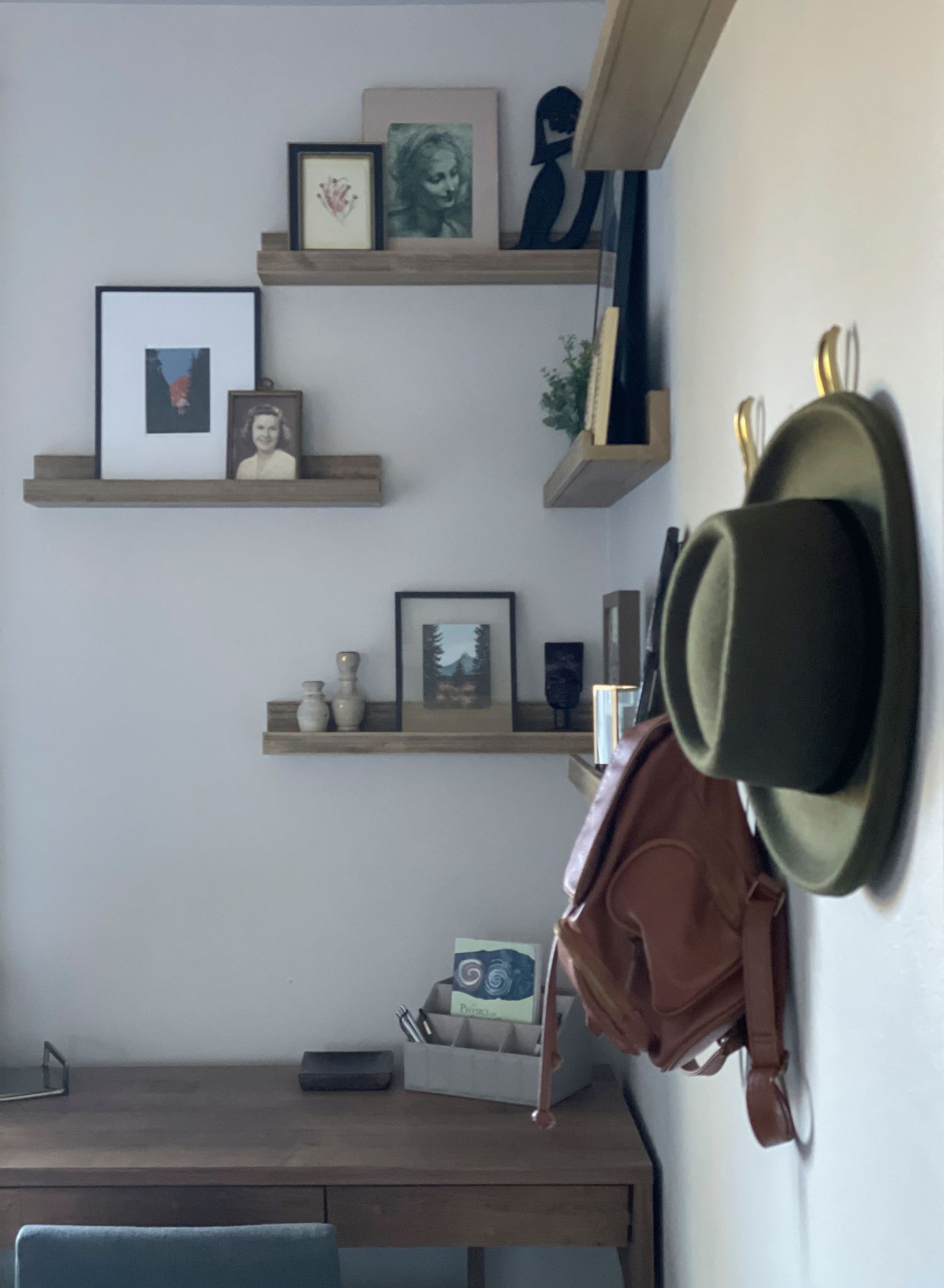 Modern wall shelf display with decorative items and a hanging hat in a minimalist white room setting.