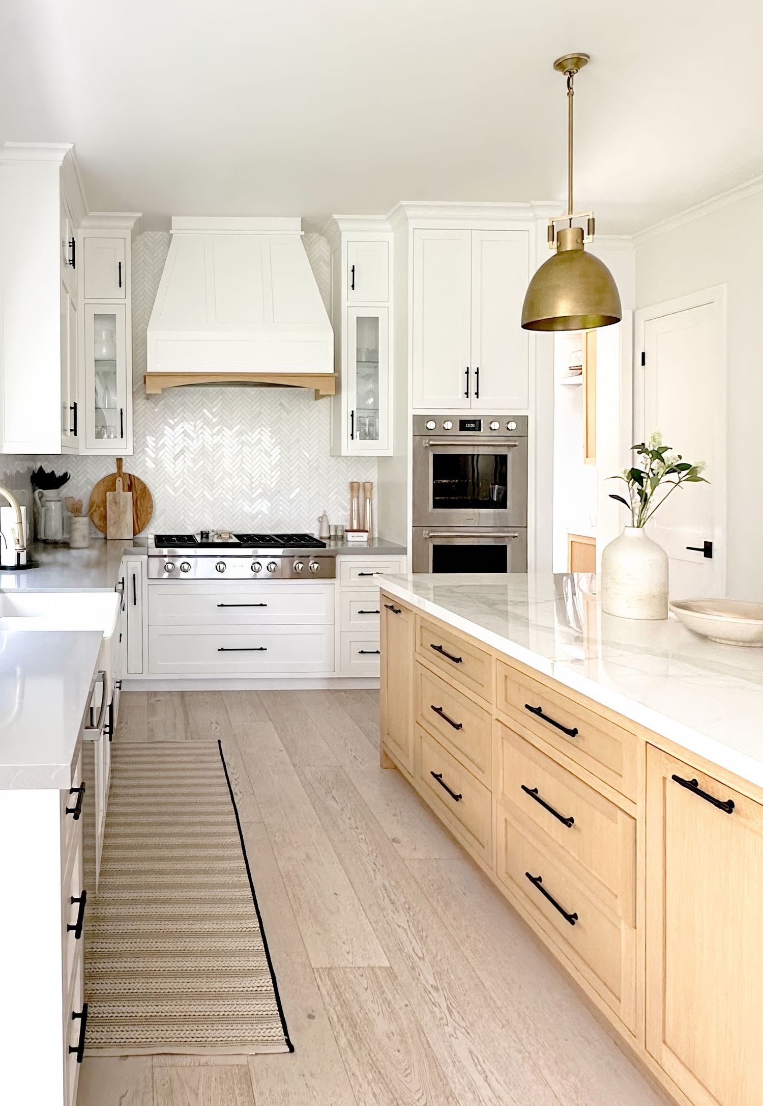 Spacious white kitchen with light wood floors, brass fixtures, and custom cabinetry.