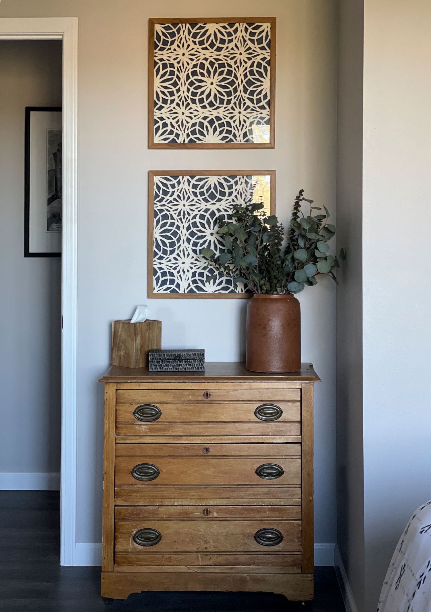Wooden dresser with decorative geometric wall art and eucalyptus in terracotta vase.
