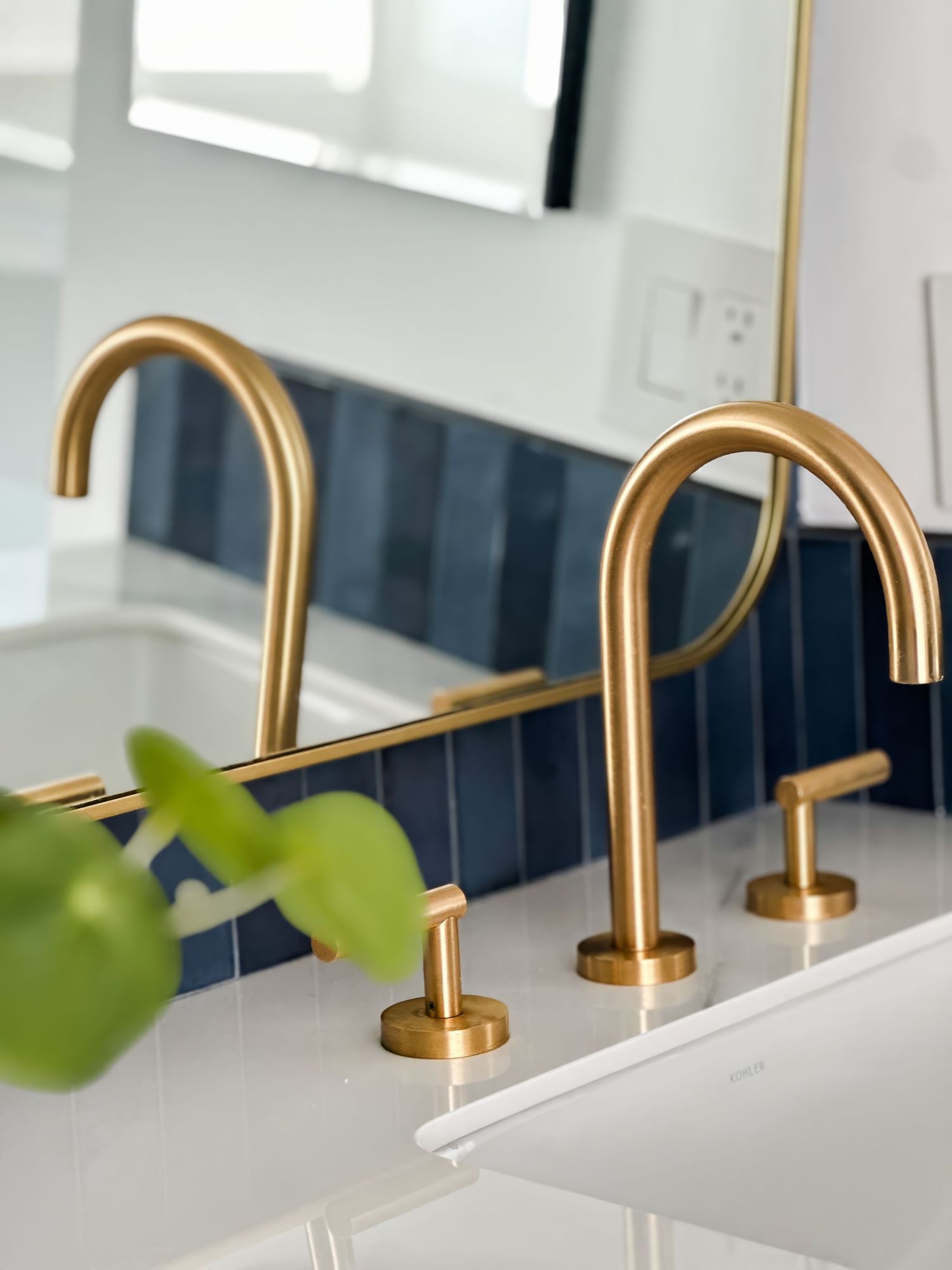 Brass bathroom faucets with curved spouts against blue tile backsplash.