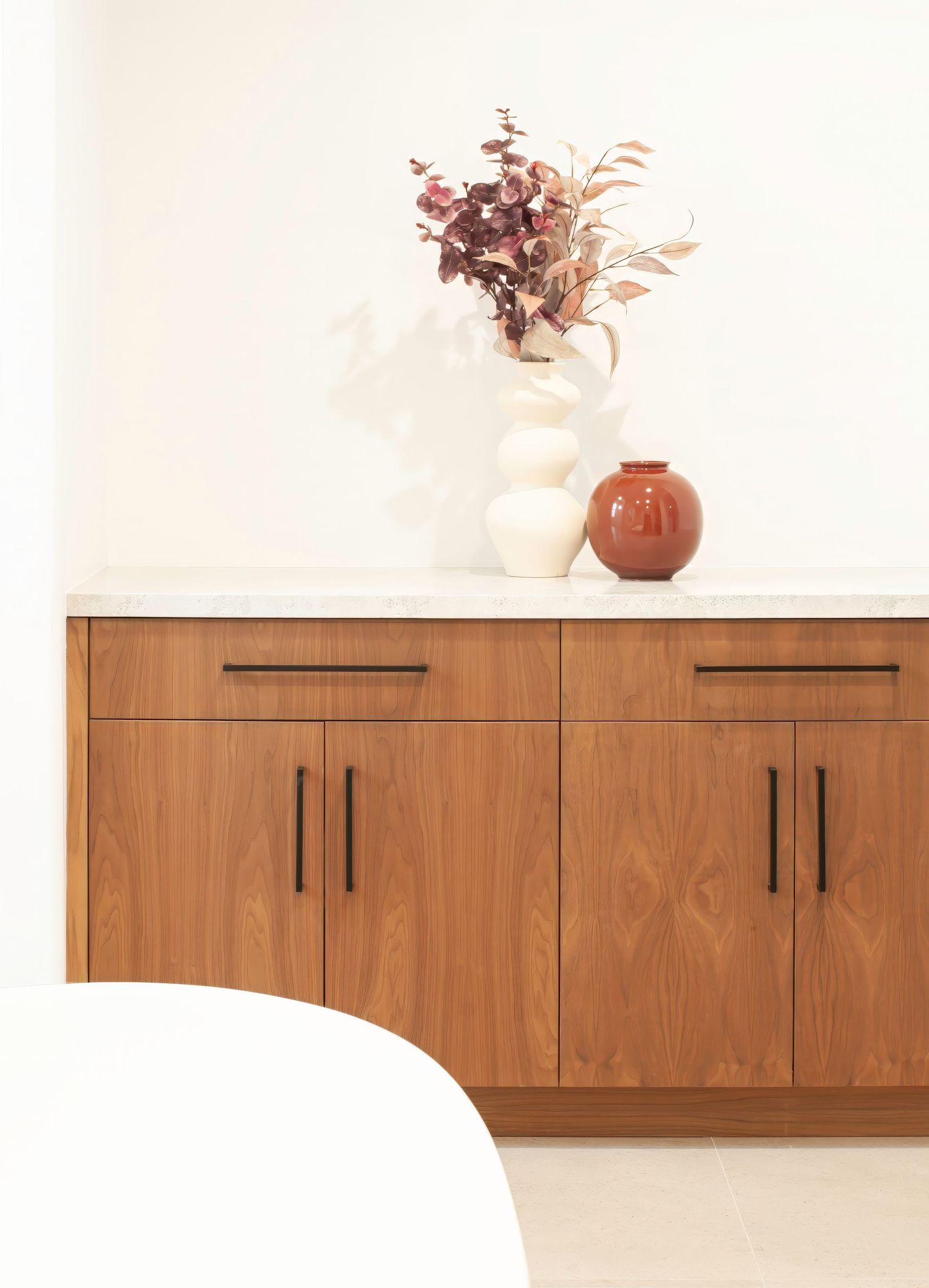 Minimalist wooden floating cabinets mounted on white wall with decorative vase on top in a bathroom suite designed by an Interior Designer.