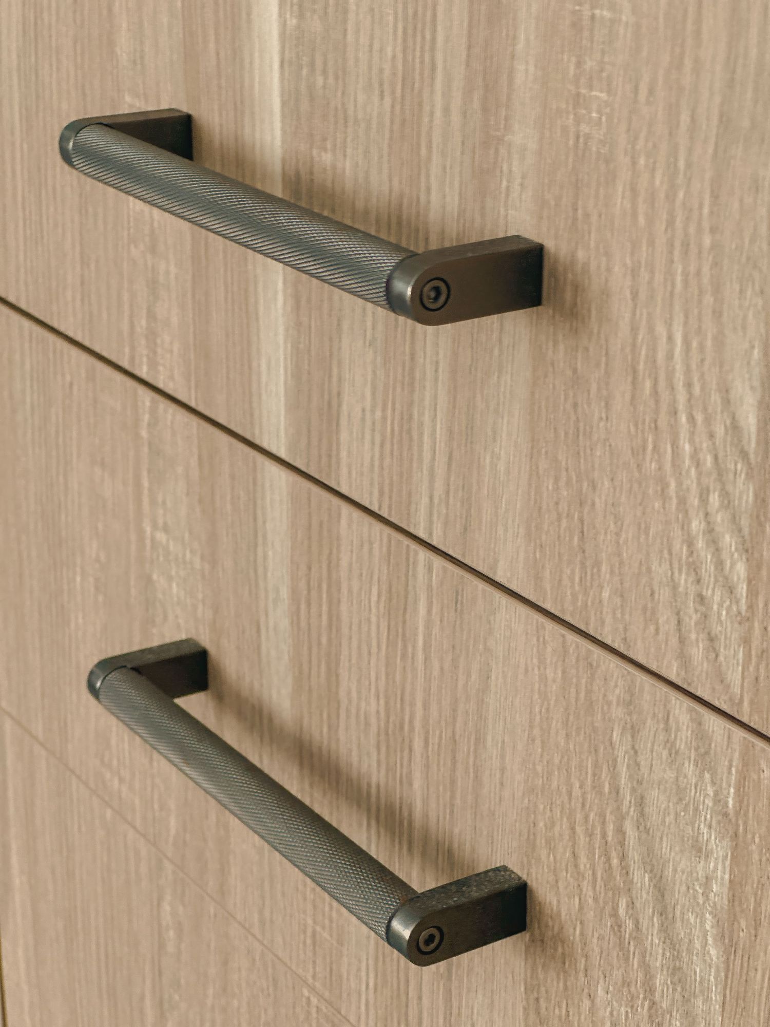 Close-up of matte black cabinet pulls mounted on light wood cabinetry.