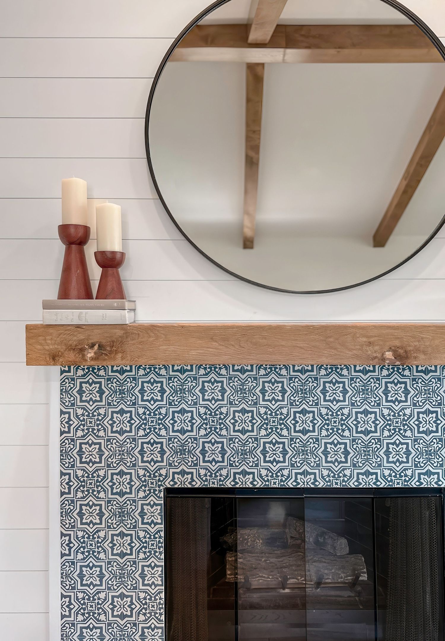Modern fireplace with blue and white patterned tile surround and round mirror above wooden mantel.