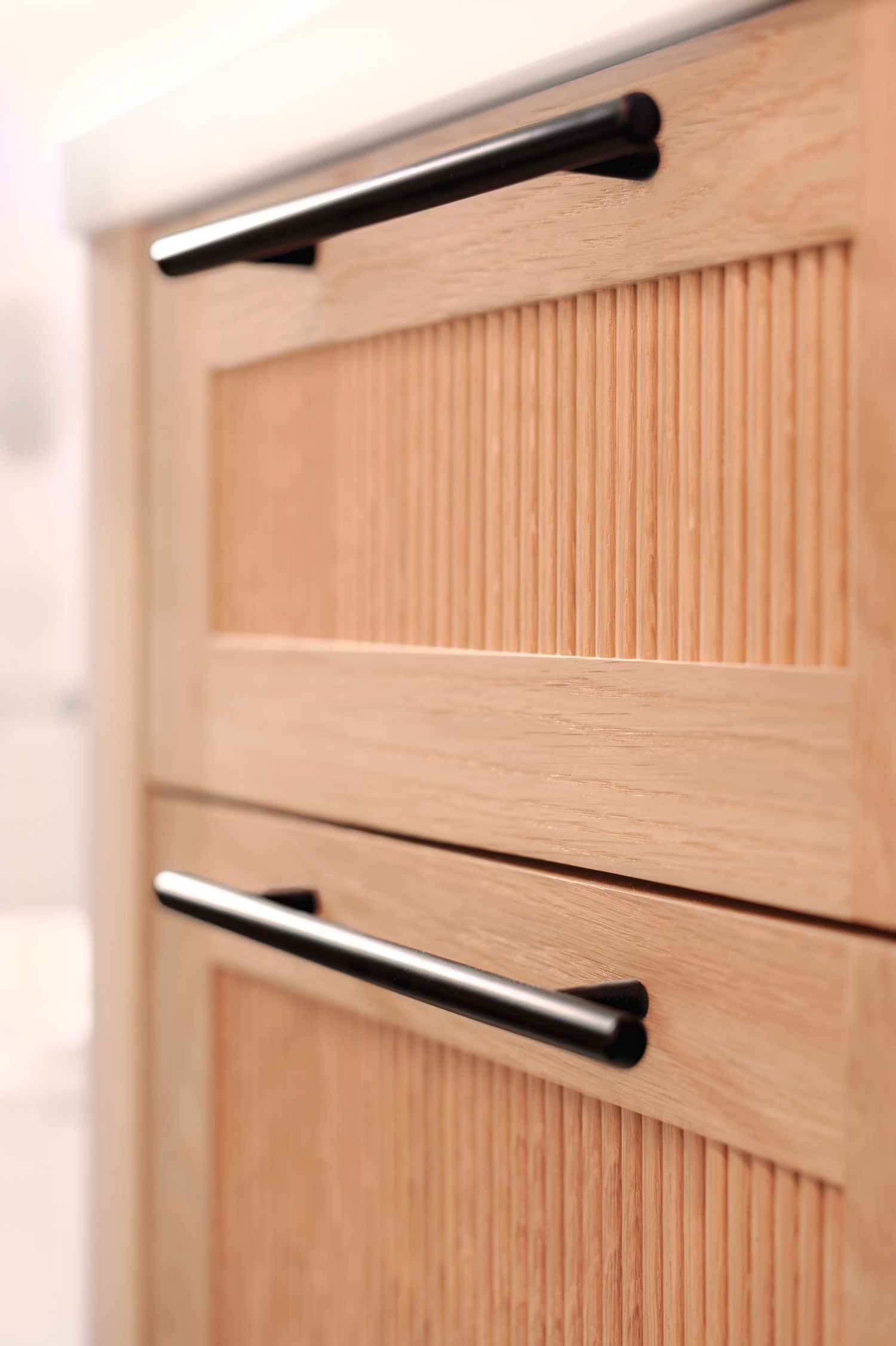 Architectural photo vignette of modern light wood reeded cabinet doors featuring sleek black horizontal handles in a minimalist design.