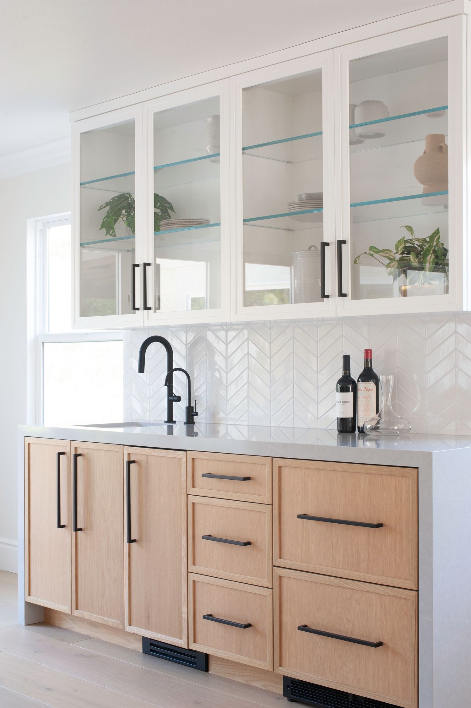 White kitchen with glass-front upper cabinets and light wood lower cabinets featuring black hardware.