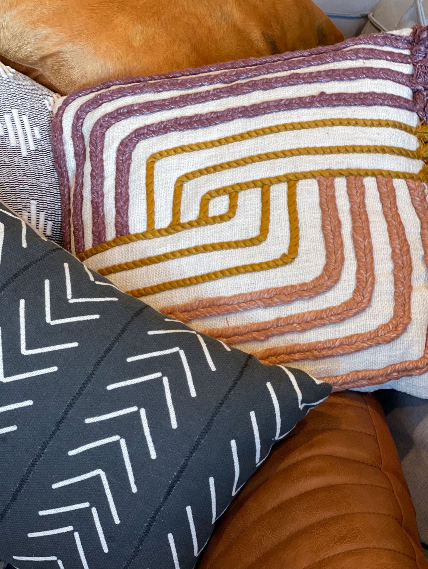 Decorative pillow with geometric patterns in brown, orange, and white stripes on dark fabric.