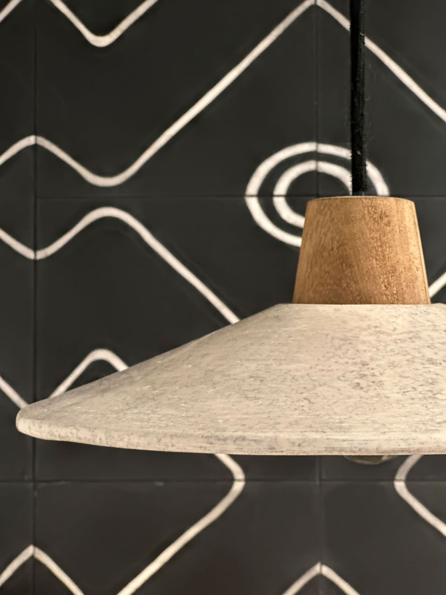Modern pendant light fixture against black wall with geometric white pattern tile in powder room.