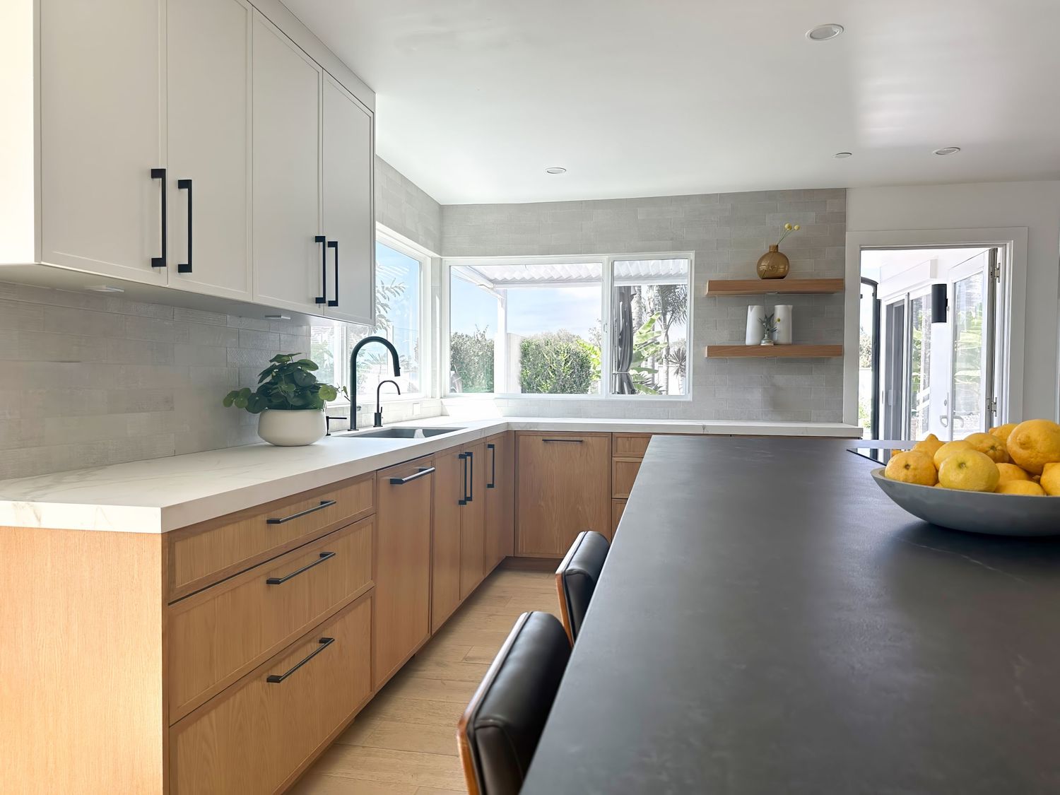 Modern kitchen with wood cabinets, black countertops and large windows.