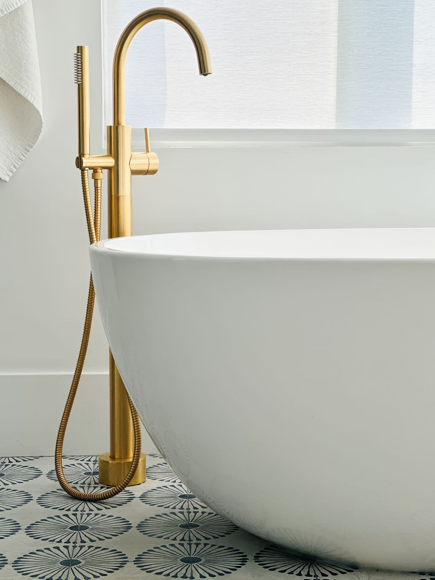 Freestanding white bathtub with brass faucet on geometric patterned tile floor.