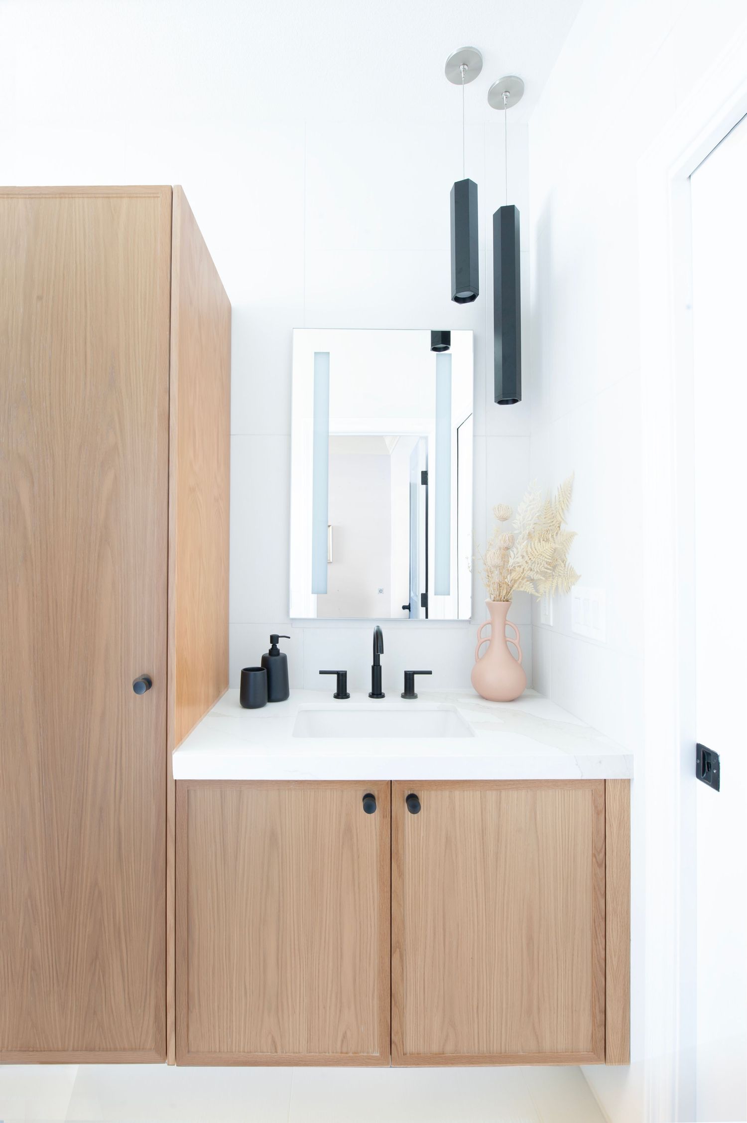 Modern bathroom vanity with light wood cabinets, black fixtures, and pendant lighting.